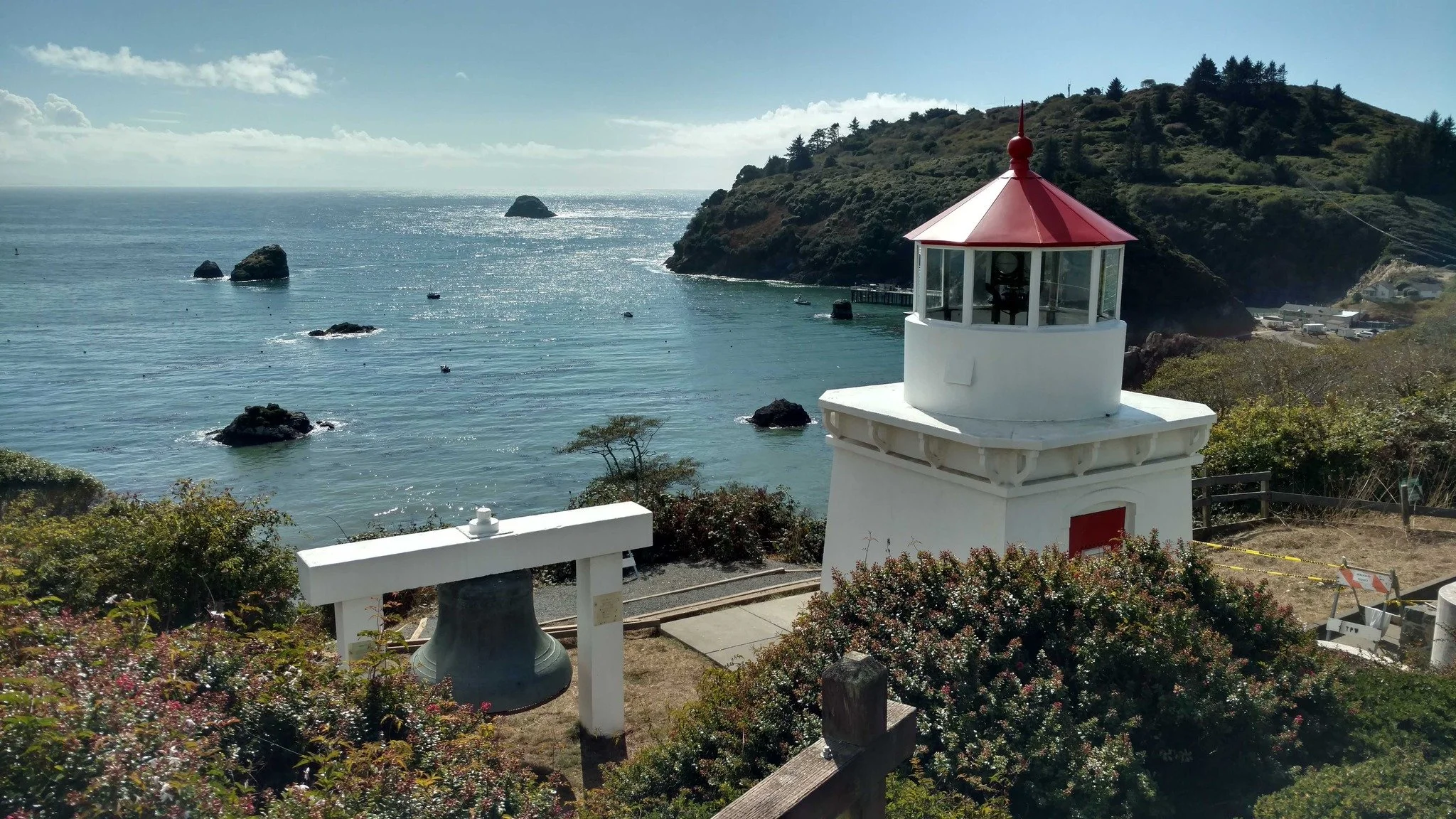 Lighthouse on a cliff overlooking the ocean with rocks in the water and a green hillside in the background