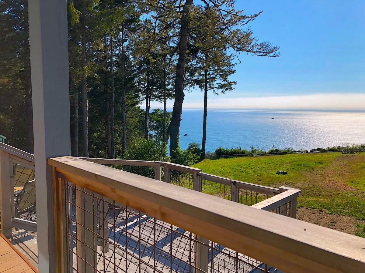 View from a balcony overlooking a grassy yard with trees and the ocean in the distance.