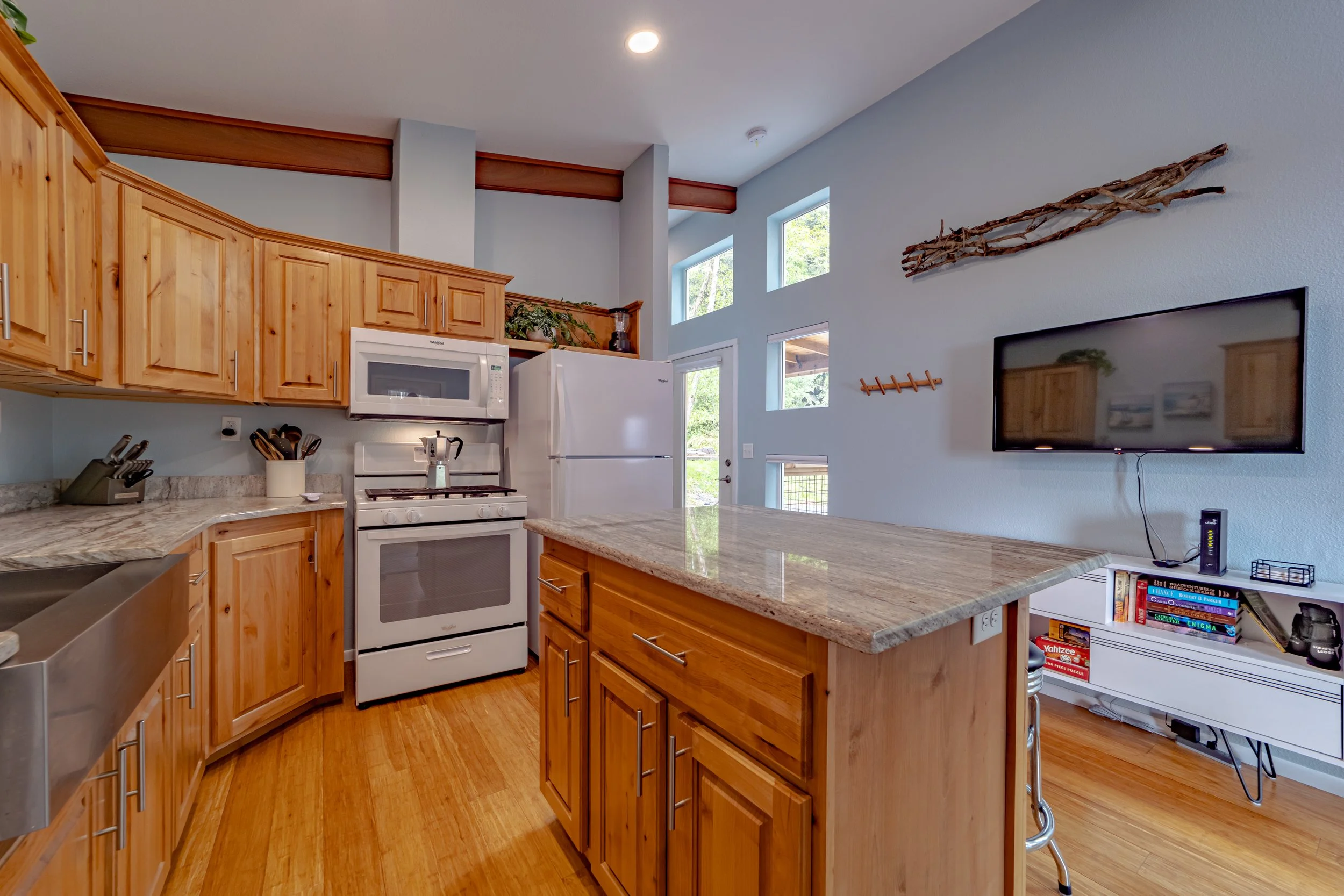 Kitchen with wooden cabinets, granite countertops, white appliances, and a wall-mounted TV on a light blue wall.