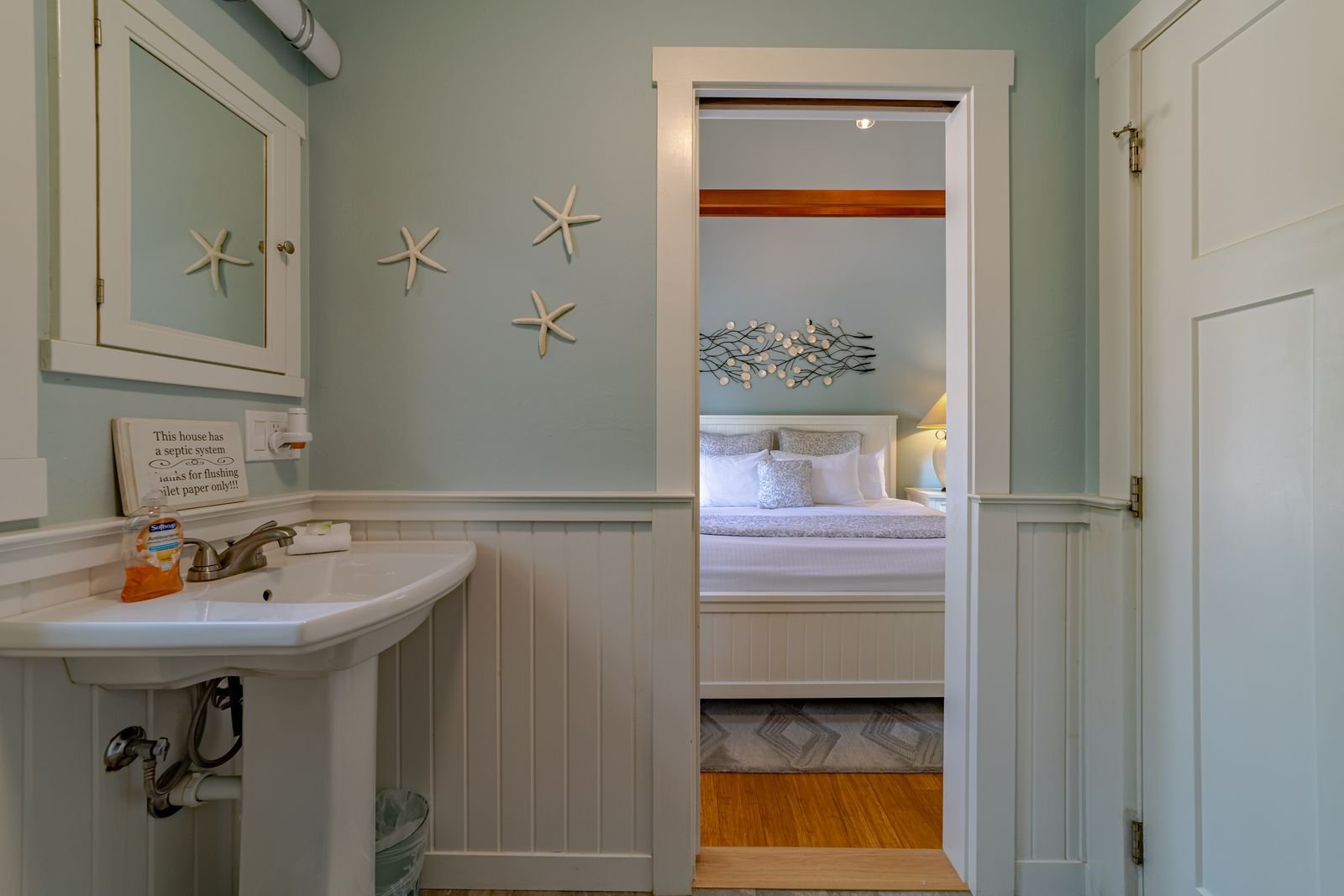 View through a doorway from a bathroom to a bedroom with a bed and wall art