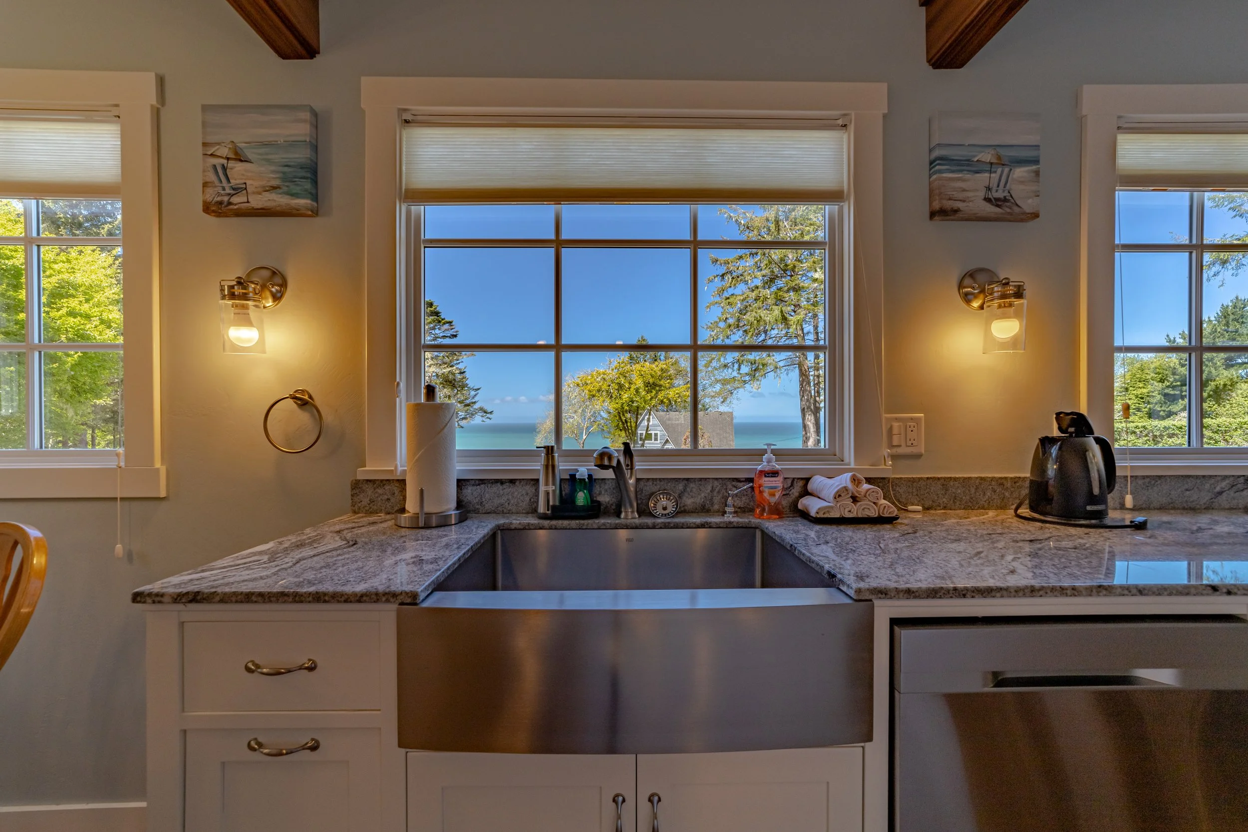 Kitchen sink area with granite countertops, a large window showing a view of trees and water, and various small appliances and decor.