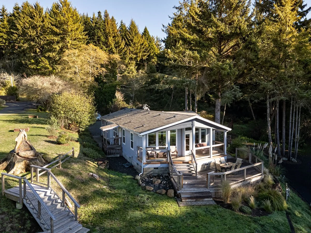 A house surrounded by trees with a wooden deck and outdoor furniture.