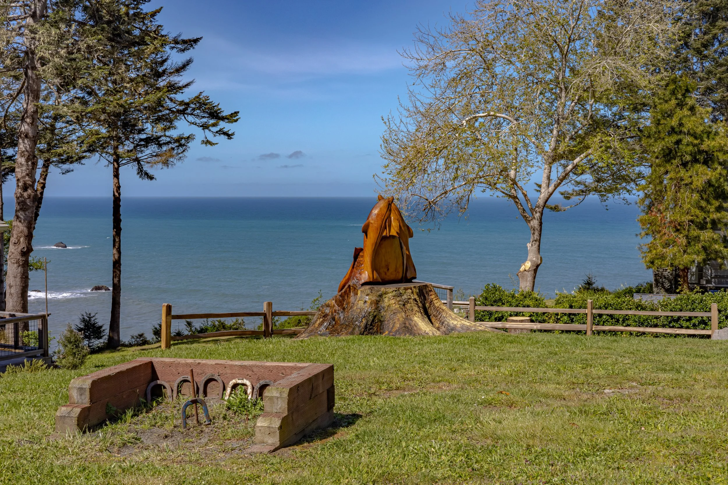 Scenic view of the ocean with trees, a carved wooden animal sculpture on a tree stump, and a brick planter in the foreground.