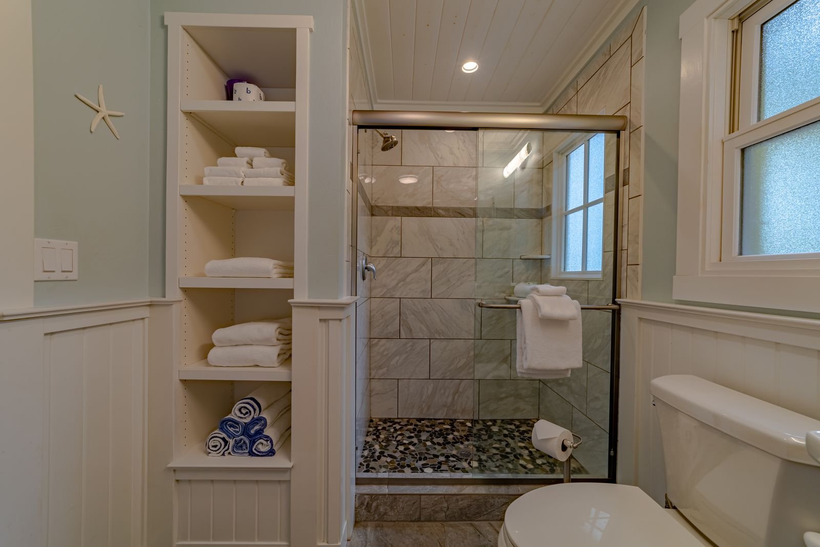 Bathroom with a walk-in shower, white towel rack, and a glass window, decorated with beachy elements like a starfish on the wall.
