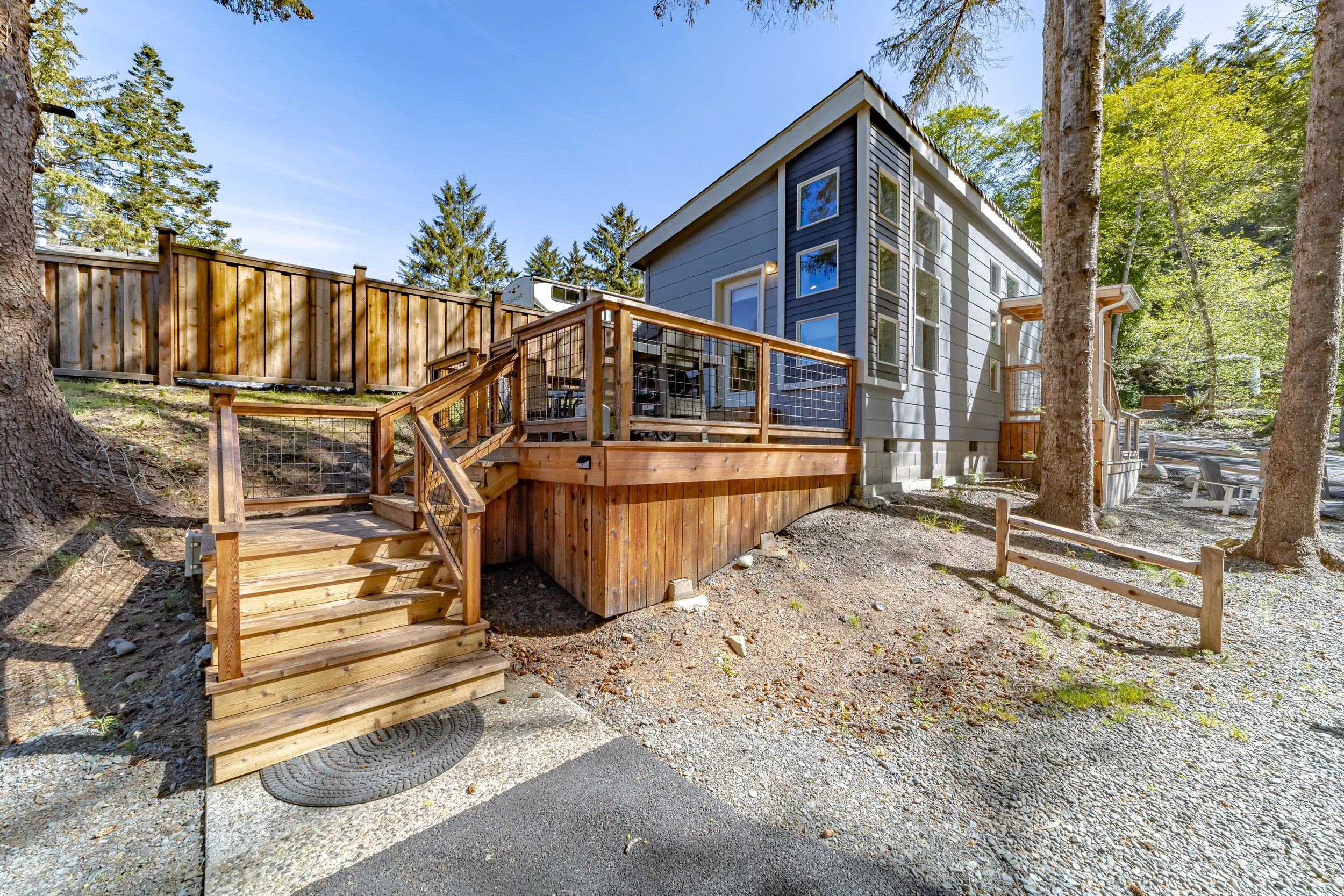 Residential house with a wooden deck, stairs, and a fenced yard surrounded by trees.