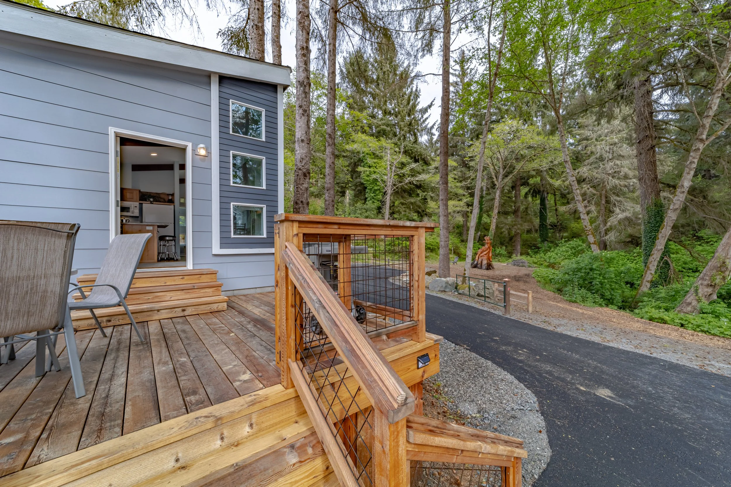 A wooden deck attached to a modern house surrounded by trees with a statue of a dog on the ground.