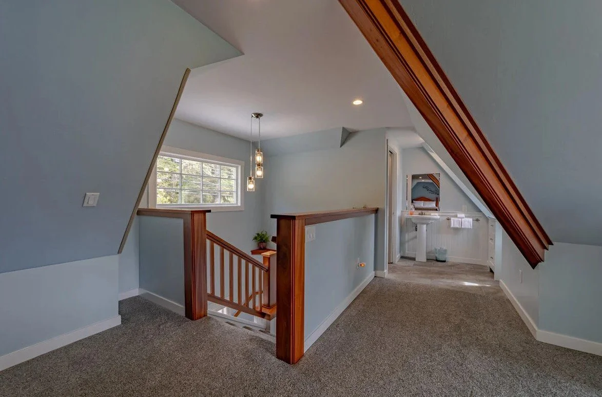 Upper floor landing area with carpeted floor, light blue walls, wooden railing, window, pendant lights, and a small bathroom with sink and mirror.