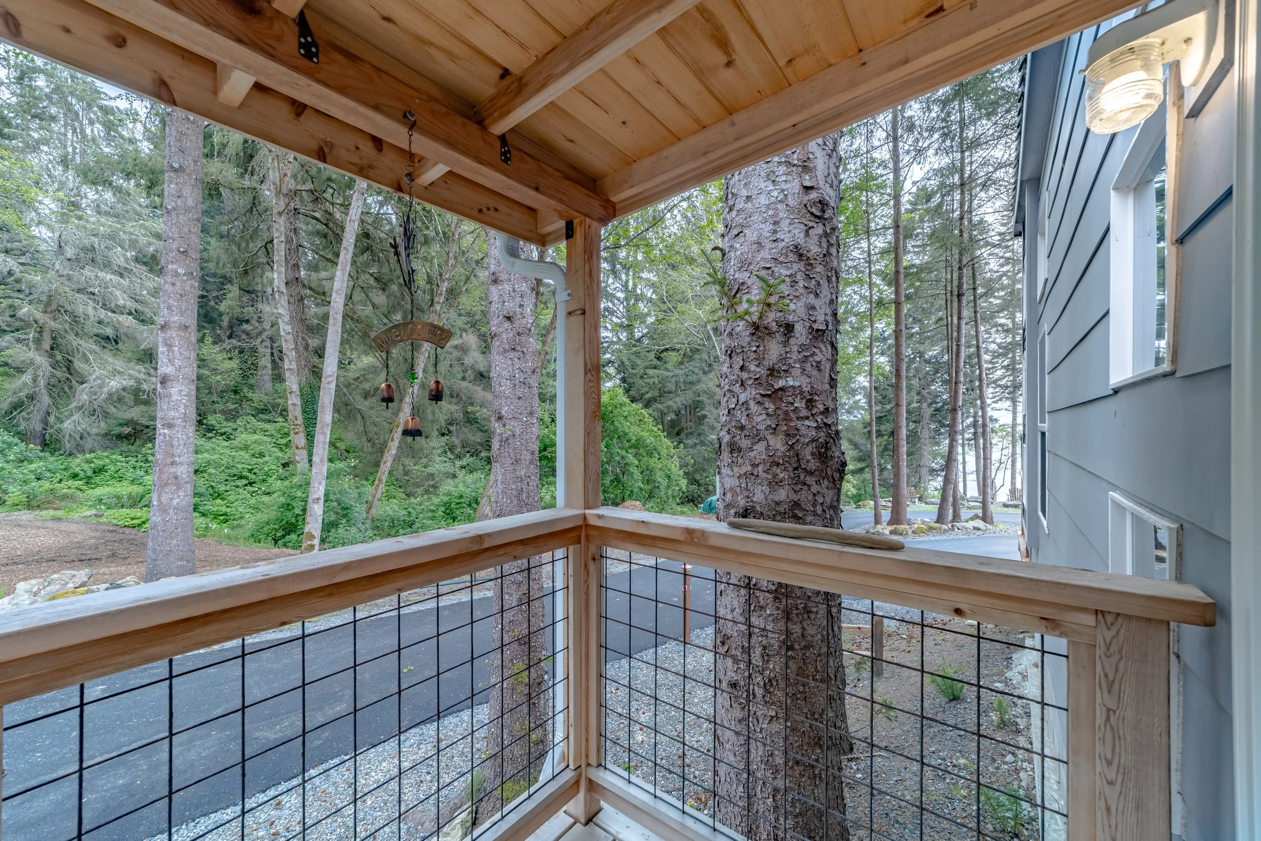 View from a wooden porch with a wire railing, overlooking a forested area with trees and a paved road in the background.