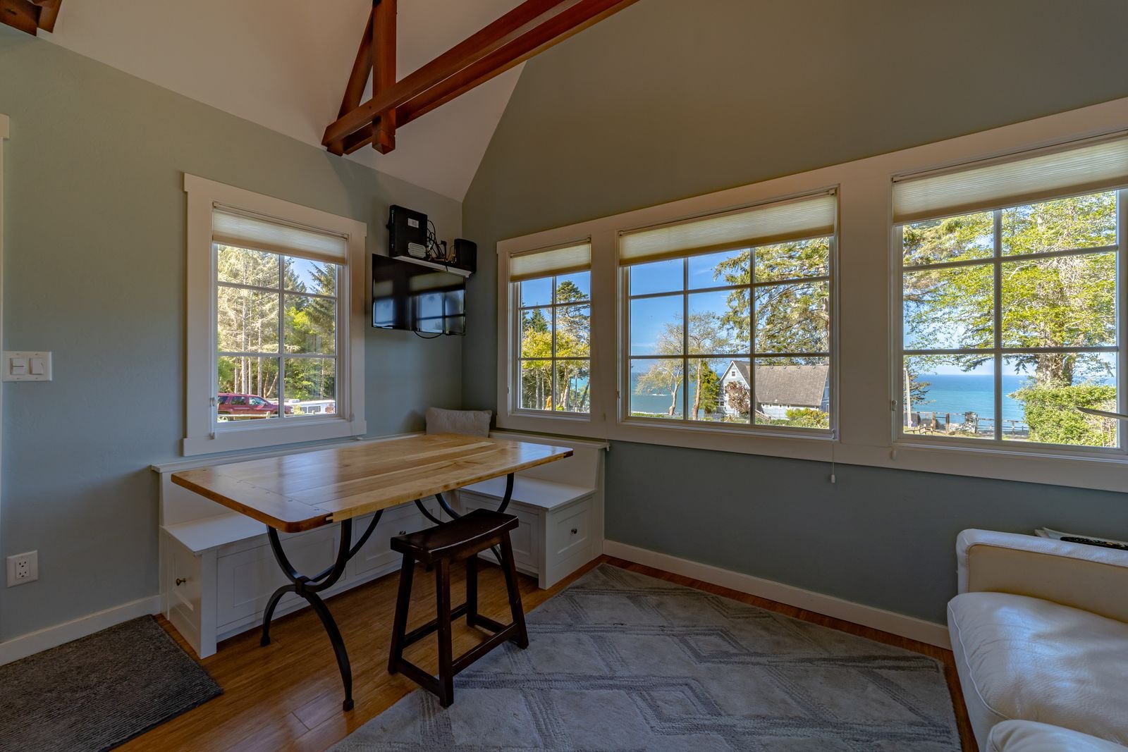 Room with large windows overlooking a lake, small desk with a chair, wall-mounted TV, and a white couch.