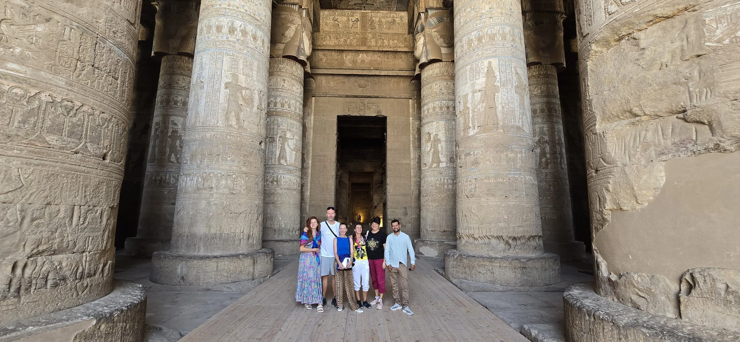 Group of six people standing in front of ancient Egyptian temple entrance with large decorated columns.