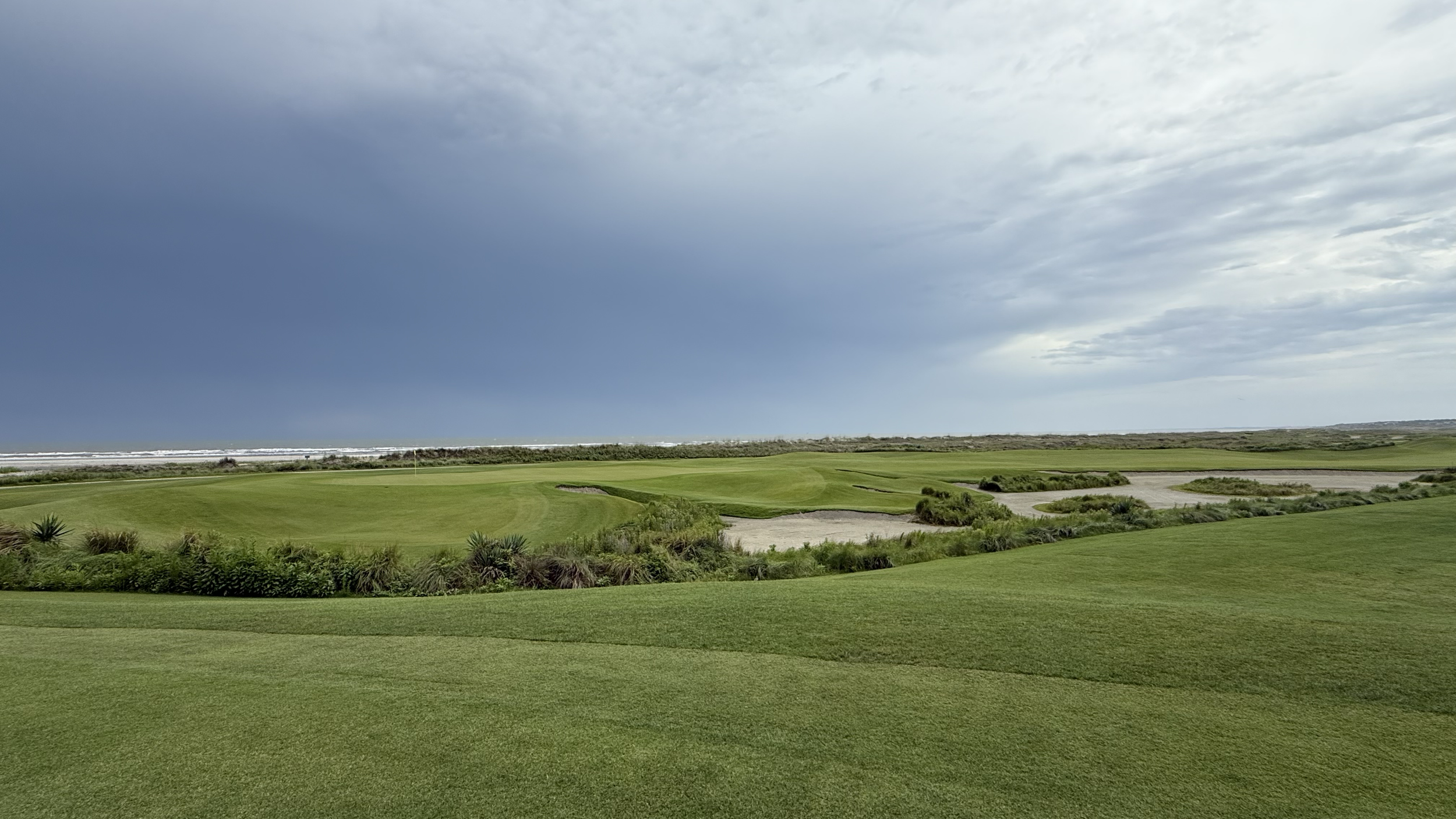 A golf course overlooking the ocean under a partly cloudy sky.