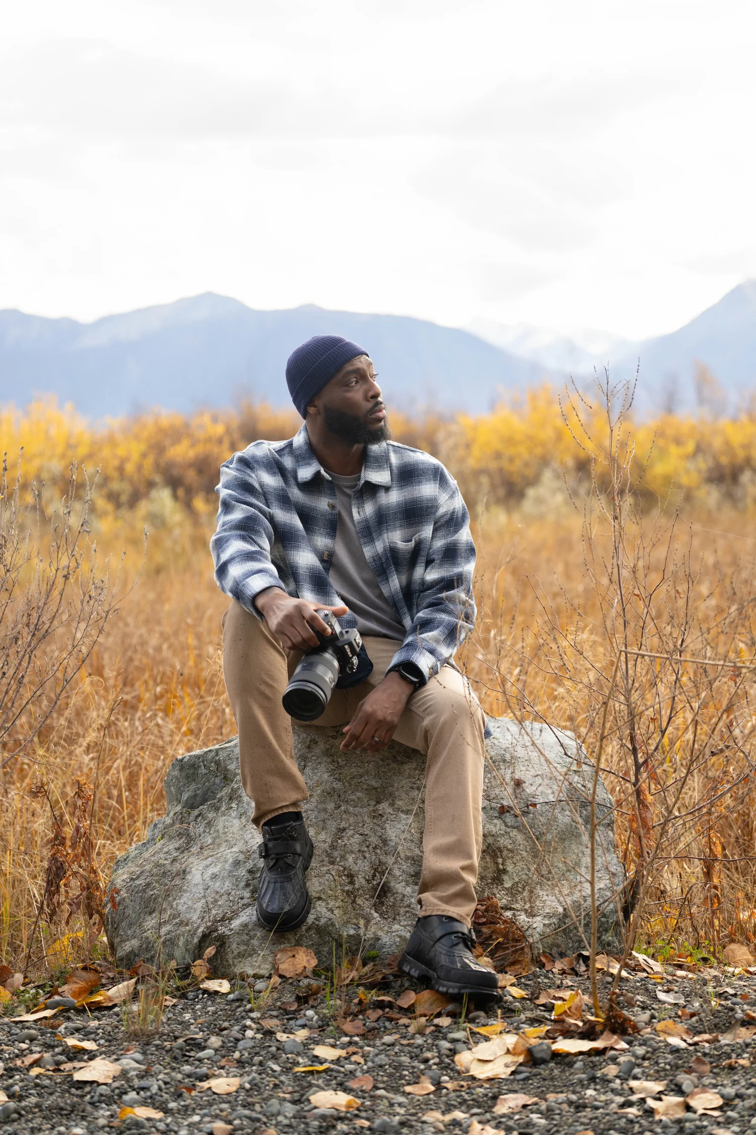 Dennis Matthews Jr. seated on a rock with his camera in a fall Alaska landscape