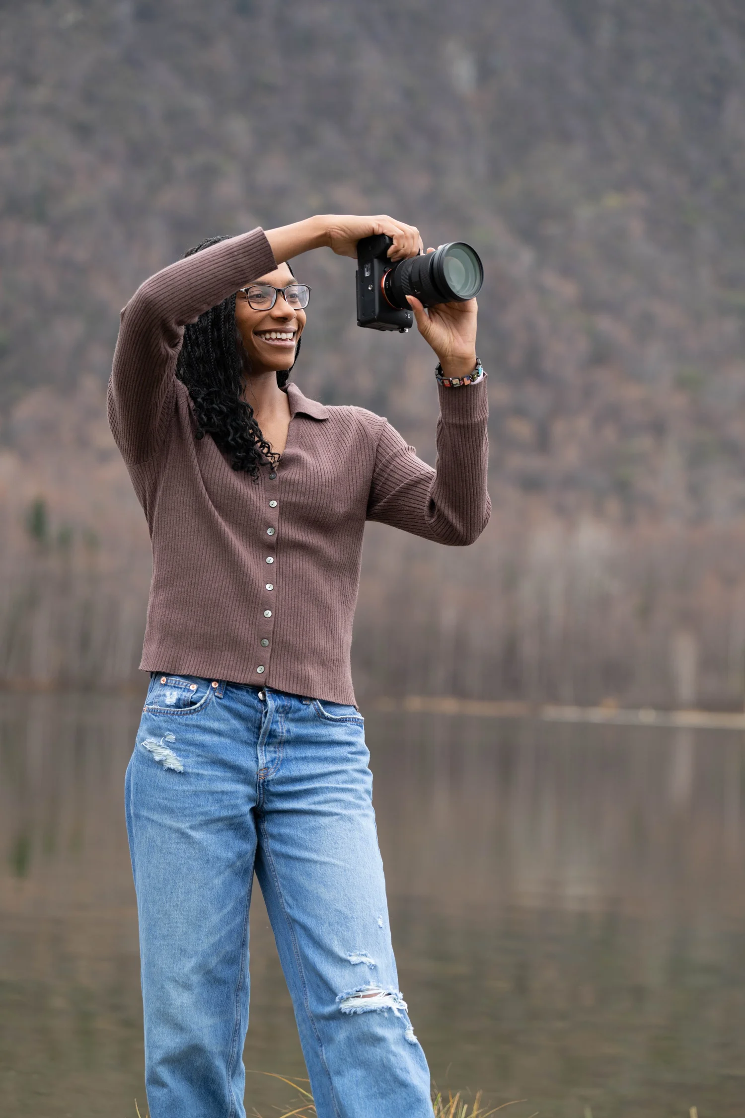 Brittany Matthews photographing outdoors near a lake with mountains in the background