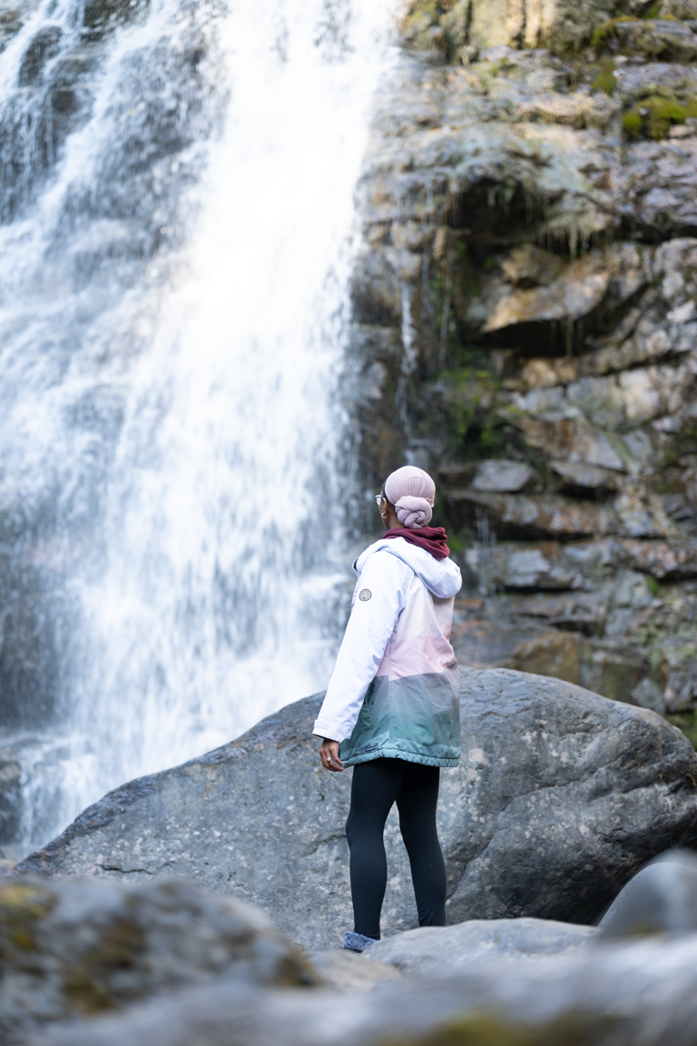 A subject stands by a rocky riverbank gazing at a waterfall, a Dot One Media production still