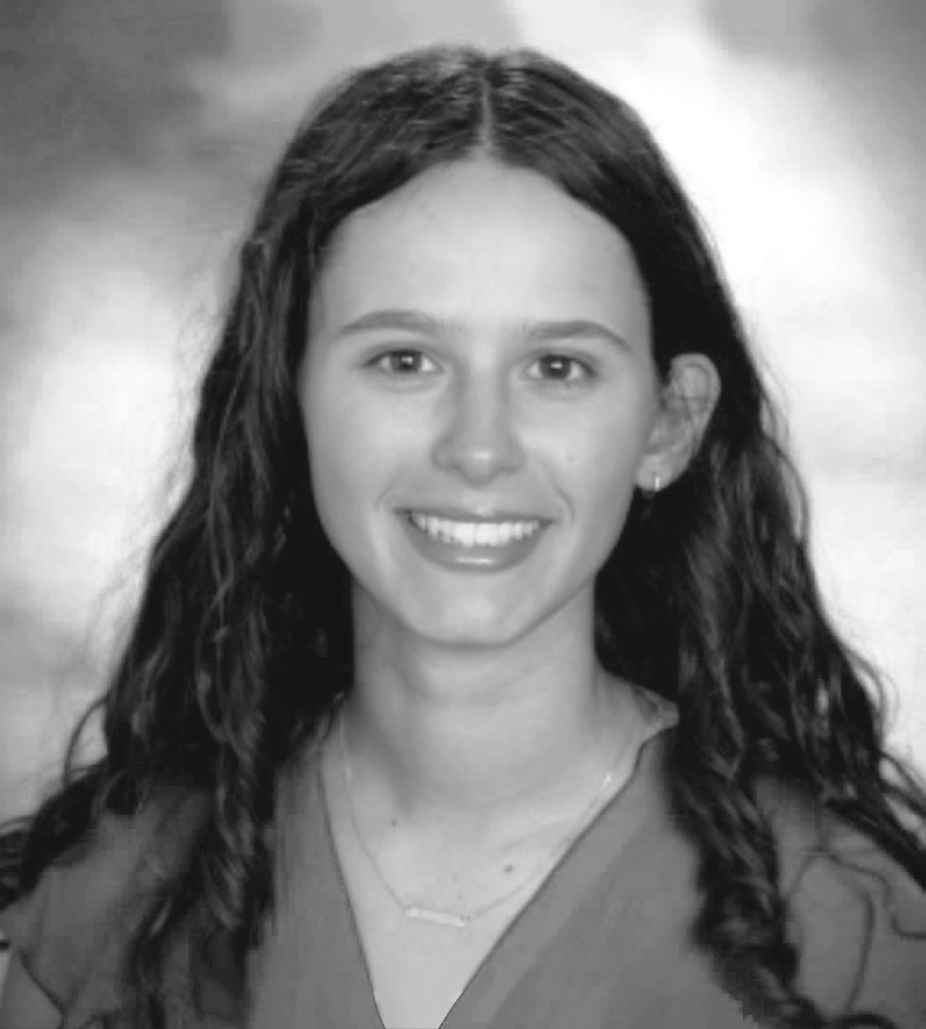 Black and white portrait of a young woman with long curly hair, smiling, wearing a necklace and earrings.