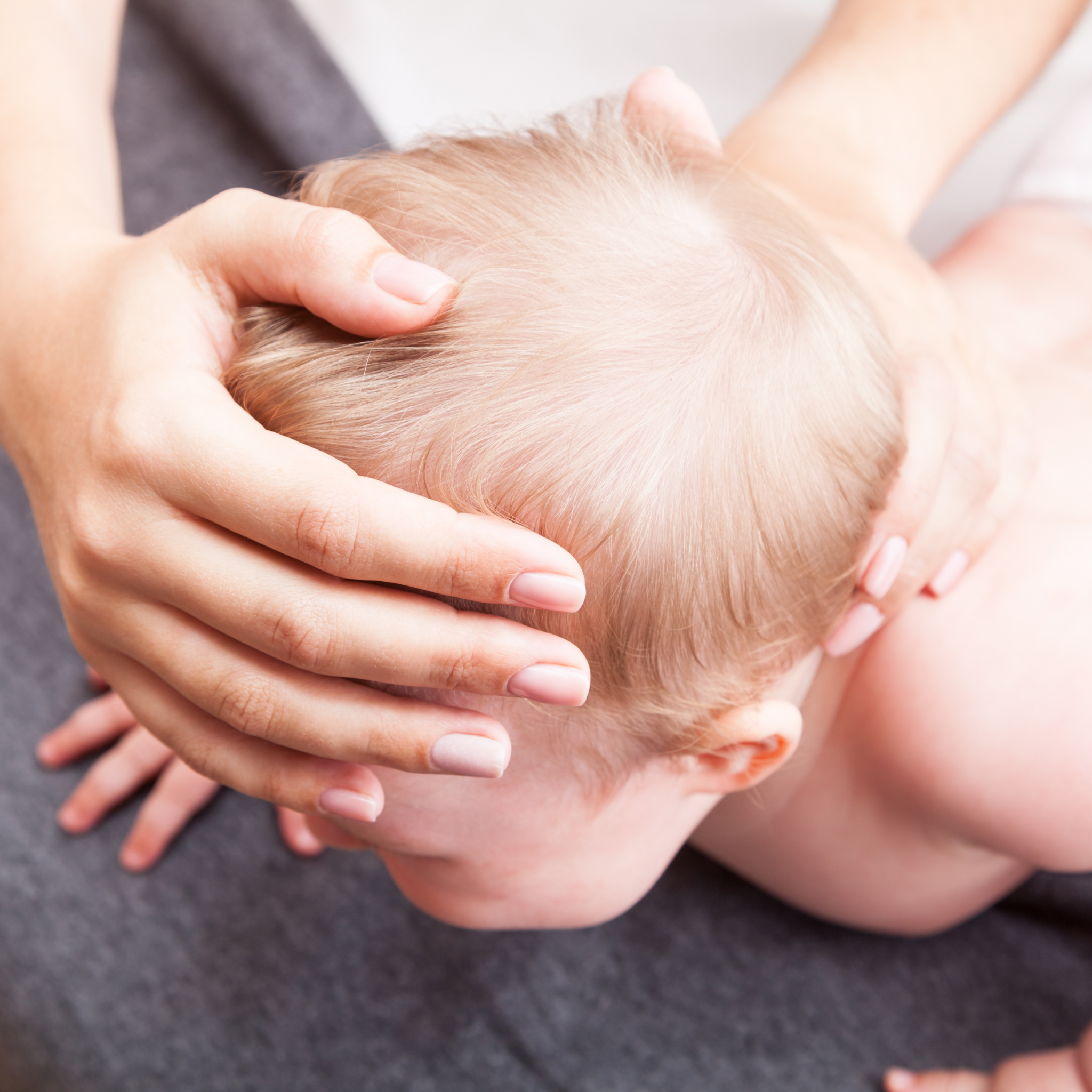 A person receiving a scalp massage from a massage therapist with hands gently on a baby's head.