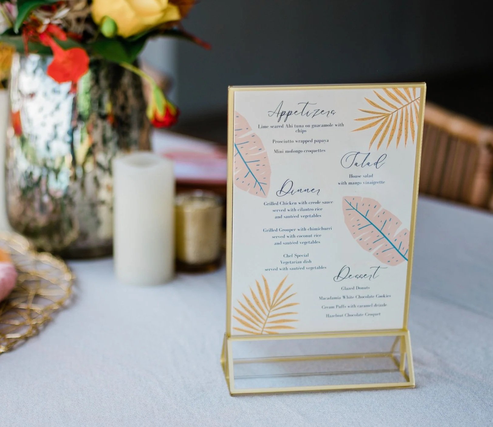 Elegant menu card on a table listing dishes for appetizers, salads, dinners, and desserts, decorated with gold and pastel leaf illustrations.