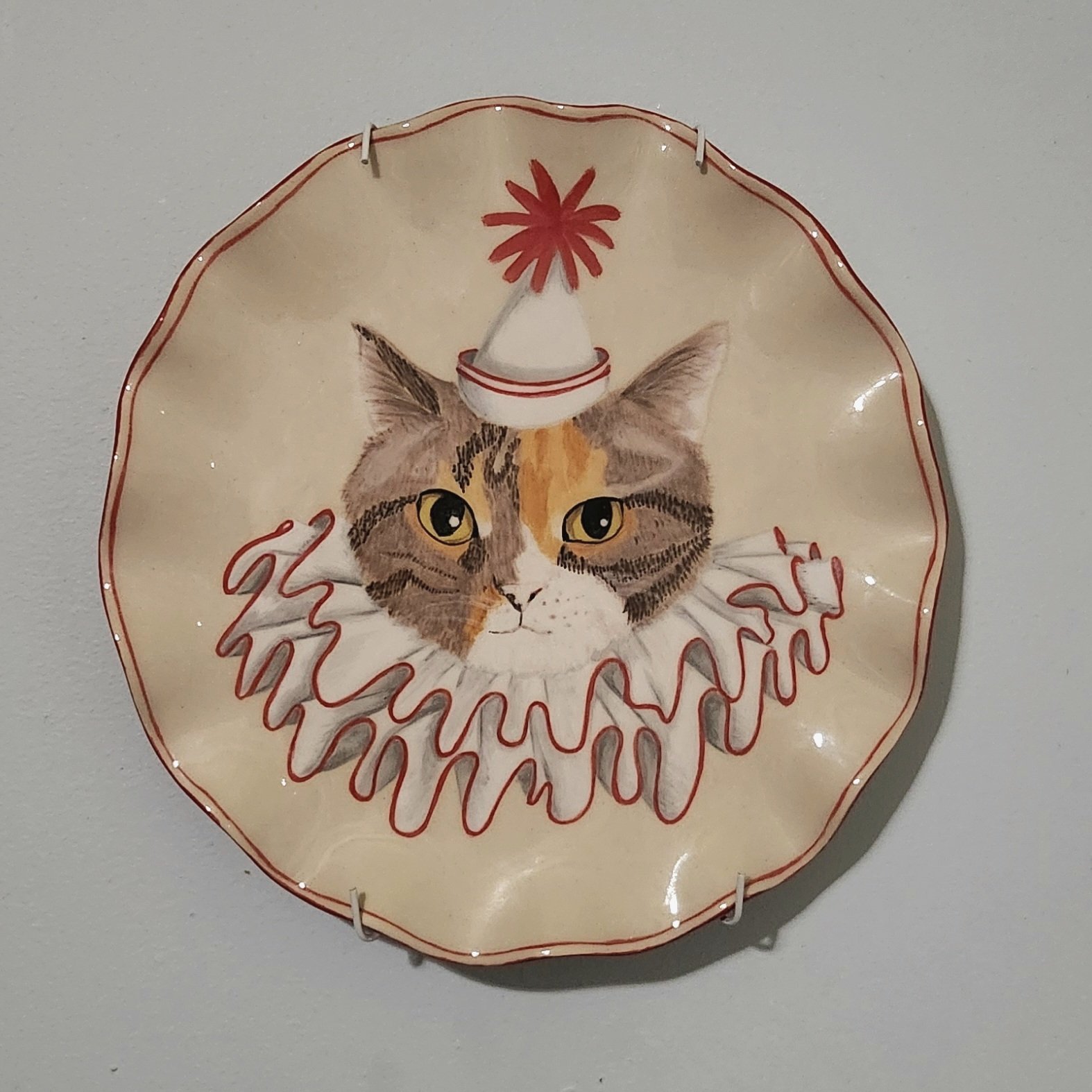 Decorative plate with a painted cat wearing a Christmas hat and a red wavy collar.