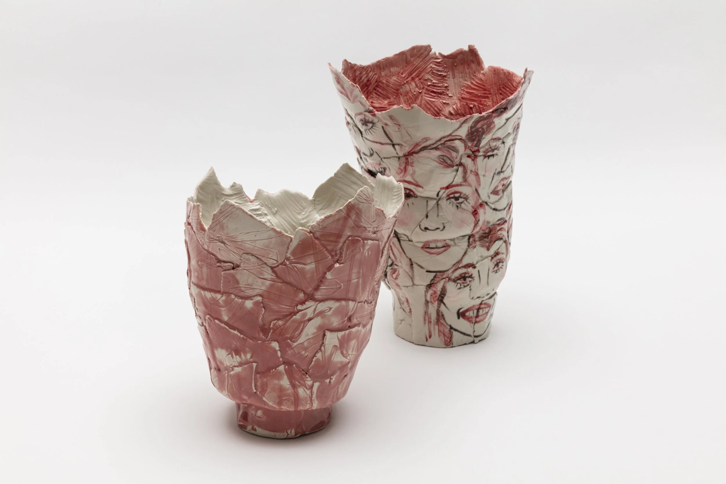 Two decorative ceramic vases with abstract and face designs, one pink and white in color, placed on a white surface.