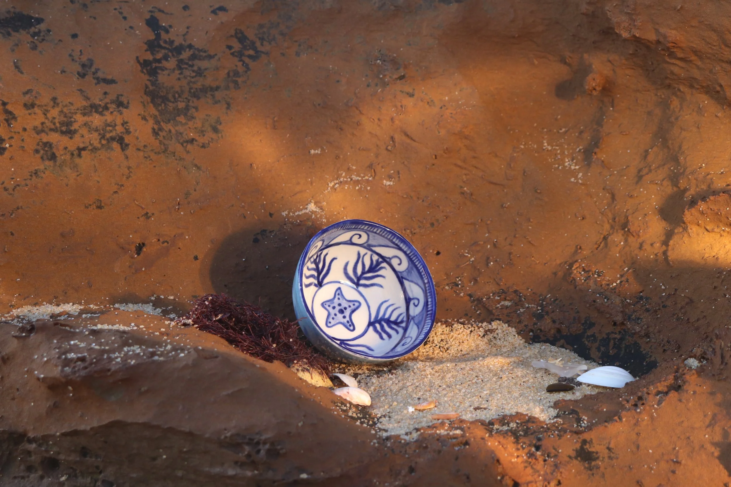 A sandy dune with a decorated ceramic bowl featuring marine themes.