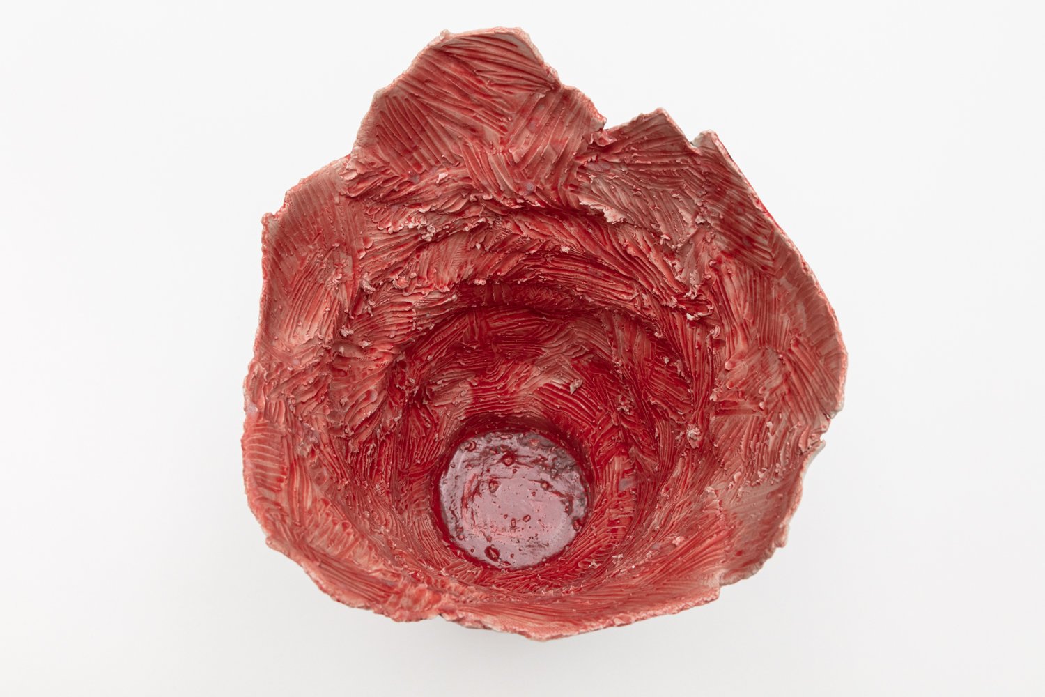 Close-up of a red vase with textured, layered surface, viewed from above on a white background.
