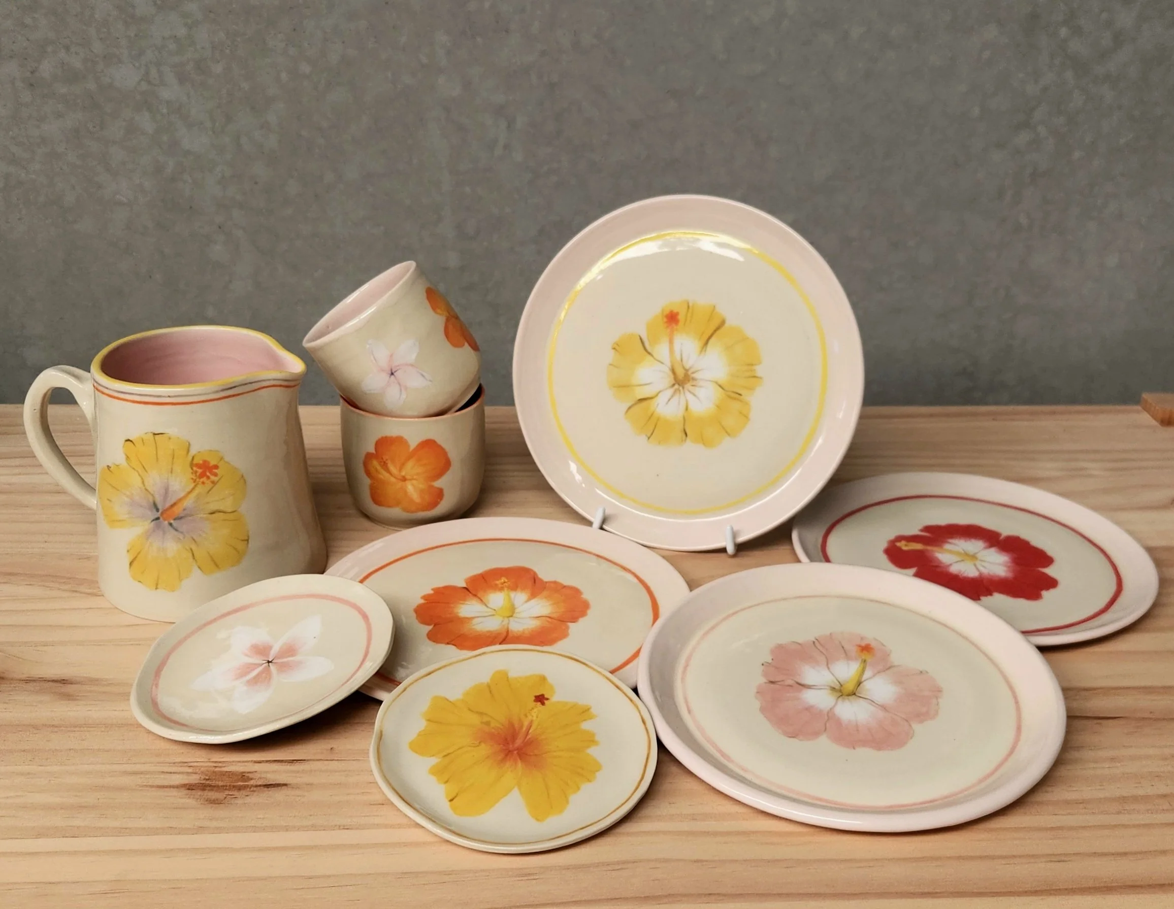 Set of ceramic tableware with floral designs, including a pitcher, cups, and plates on a wooden surface.