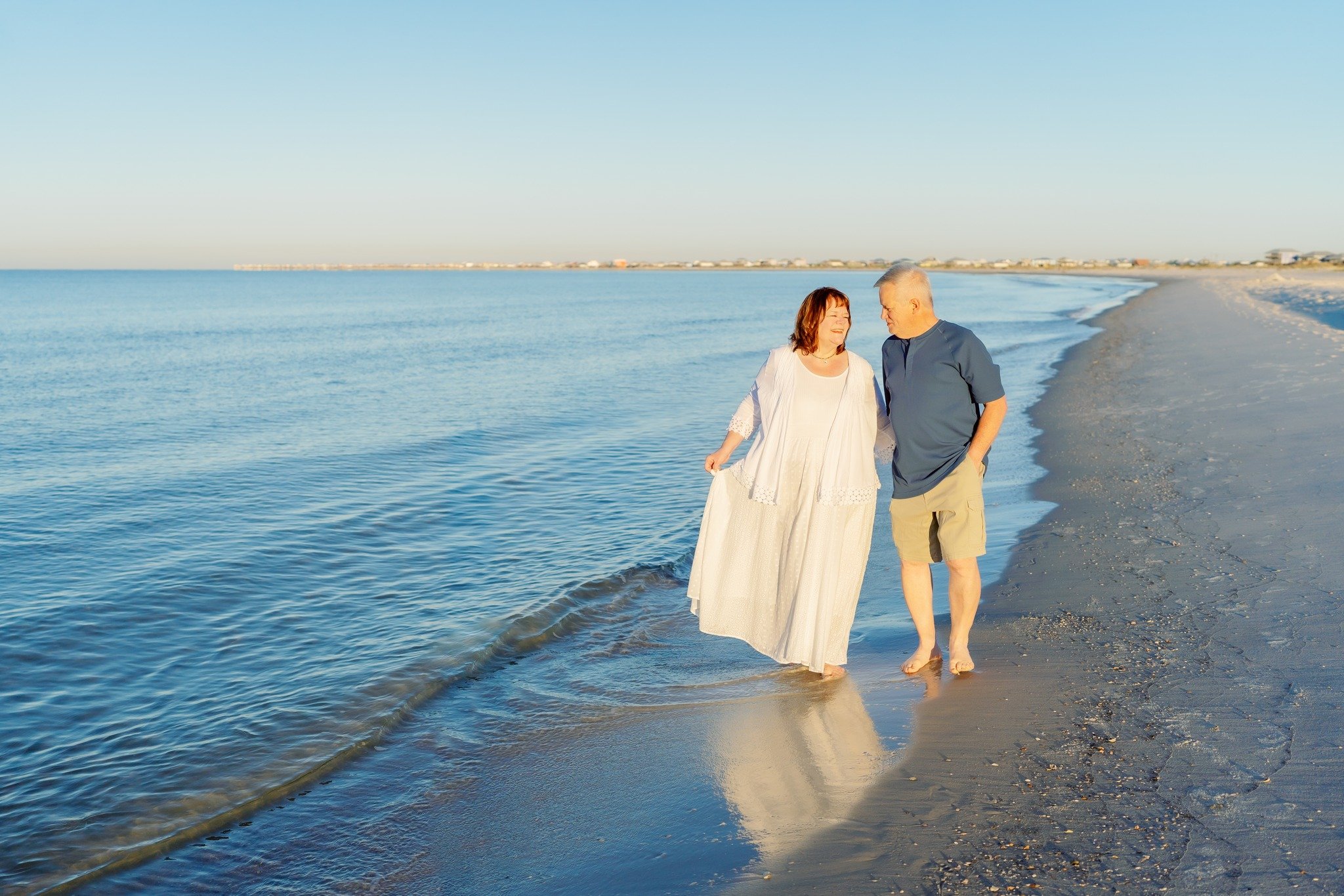 A couple walking along a sandy beach by the Gulf on Dauphin Island.