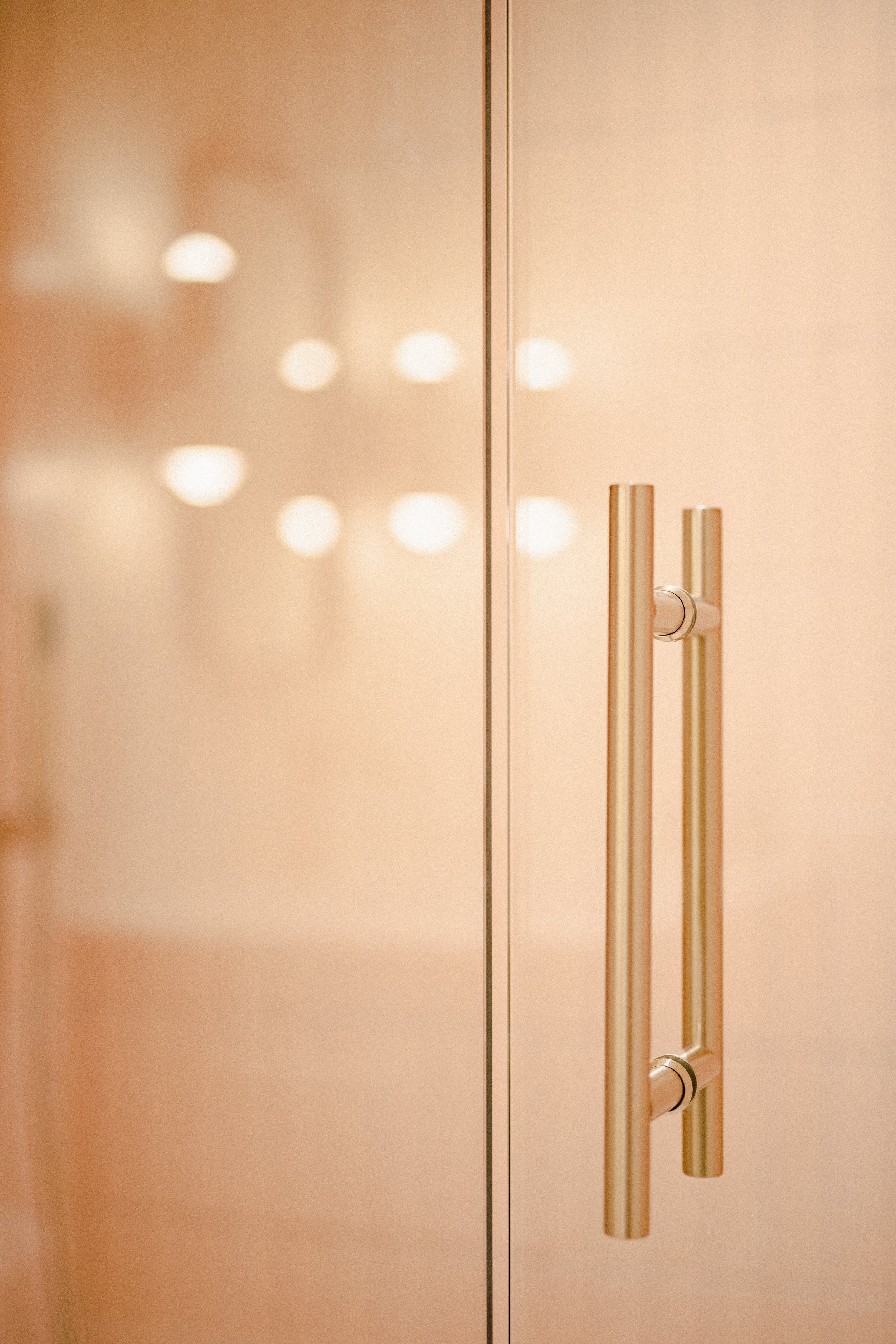 A wall-mounted mirror with a reflection of three orange hooks with gold tips in a room with warm lighting.