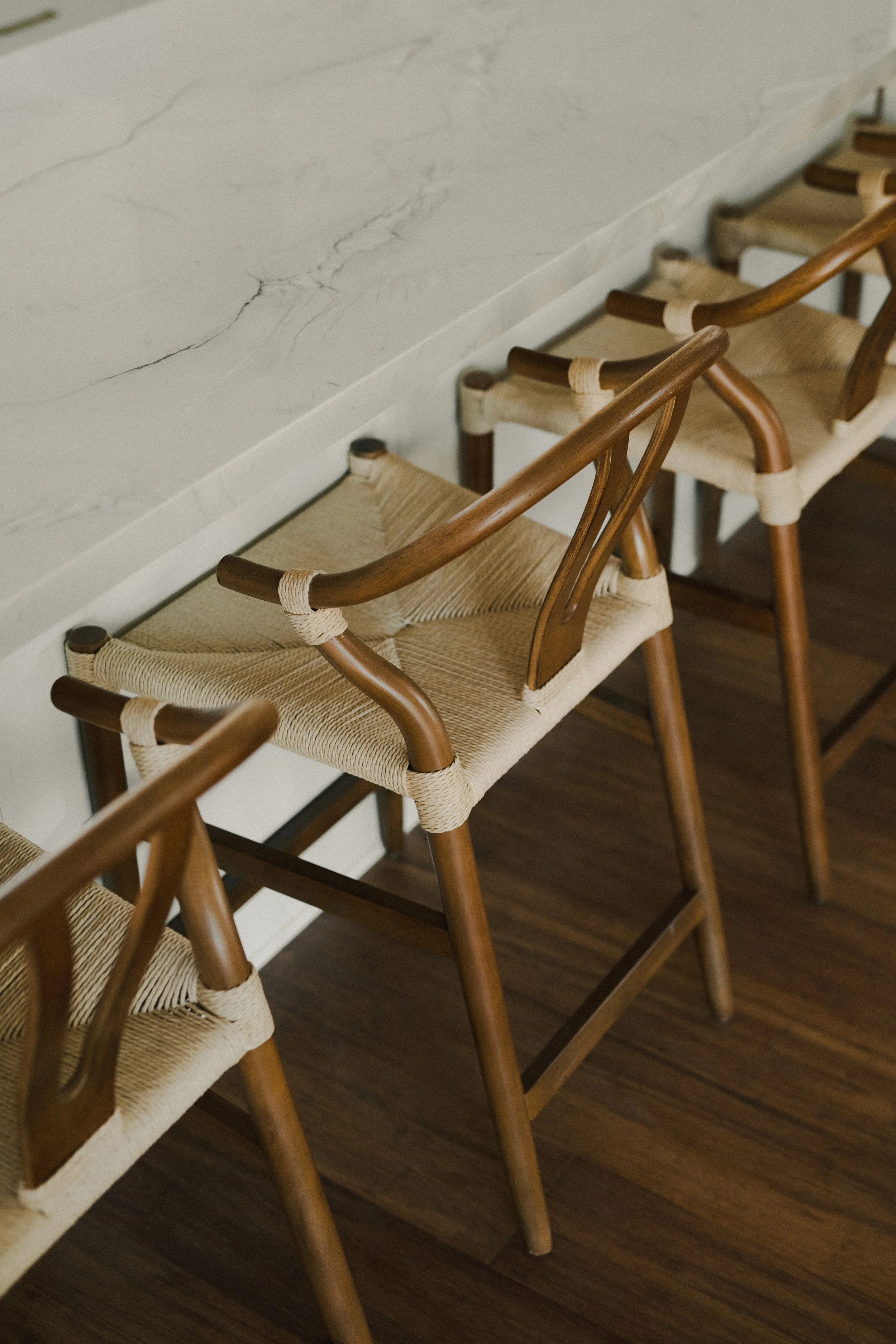 Wooden barstools with woven seats lined up against a marble countertop.