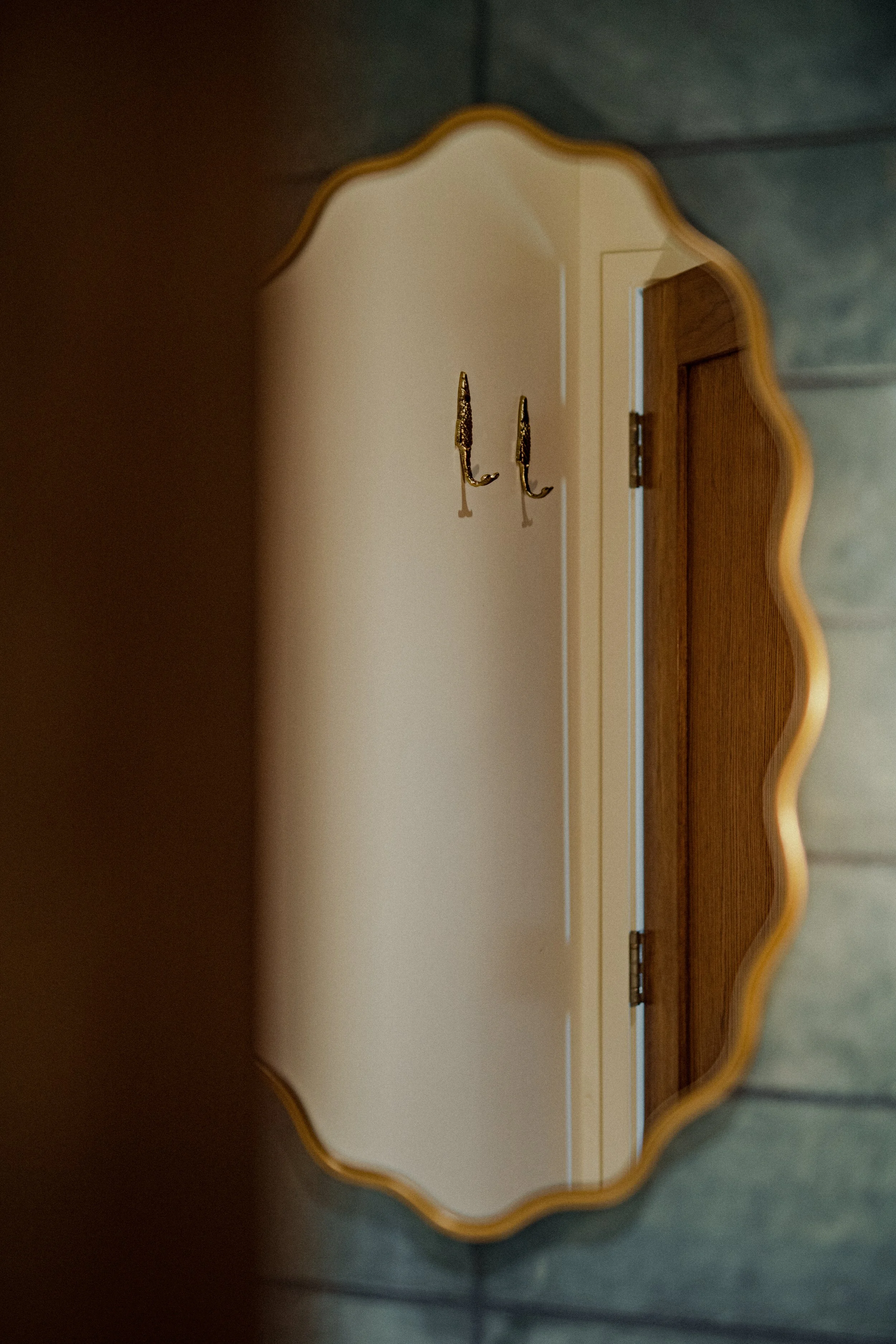 Decorative mirror reflecting a hallway with two wall-mounted hooks.