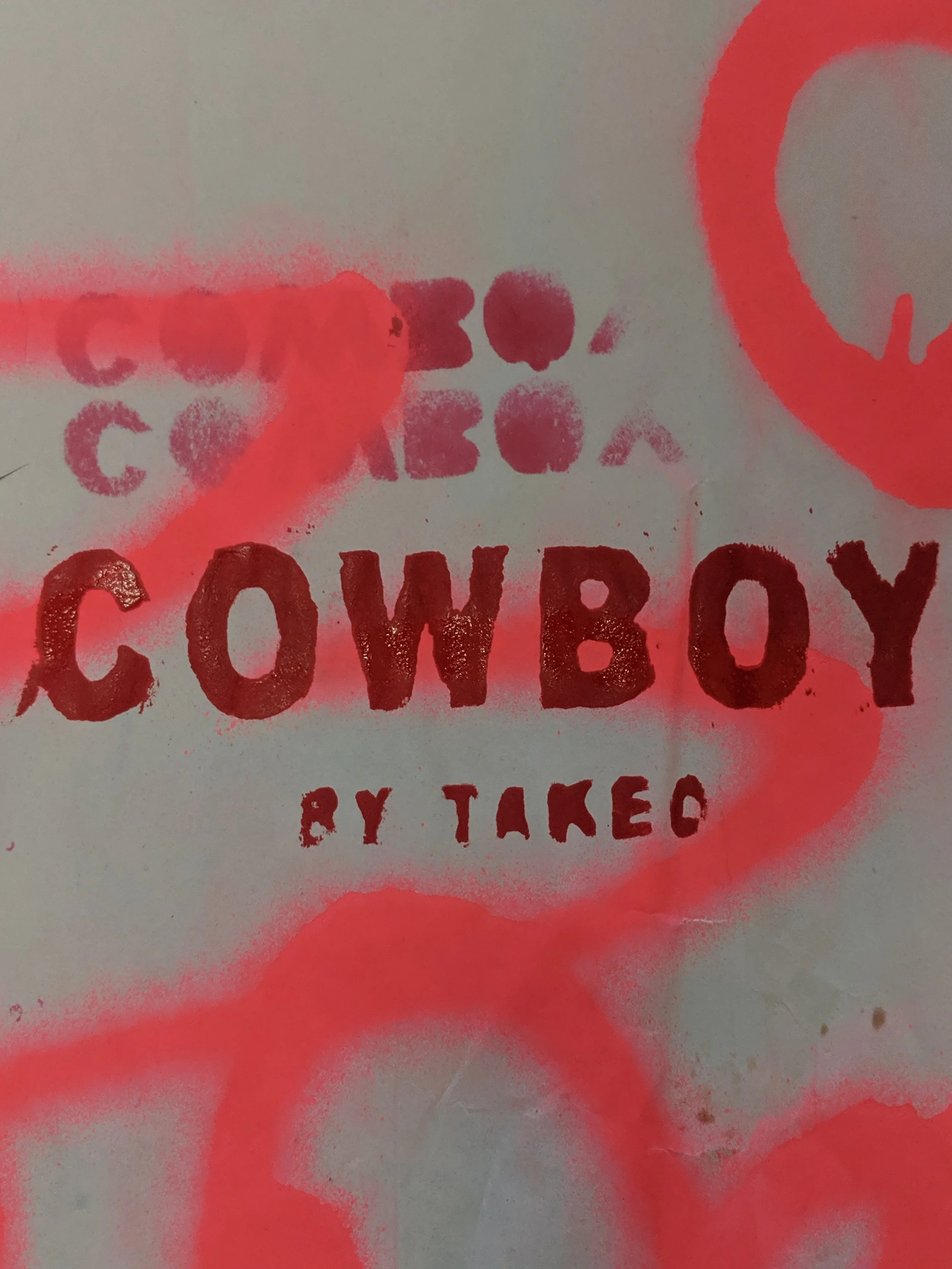 Close-up of graffiti-style text reading 'COWBOY BY TAKED' on a wall, with red spray paint and various overlapping marks and circles.