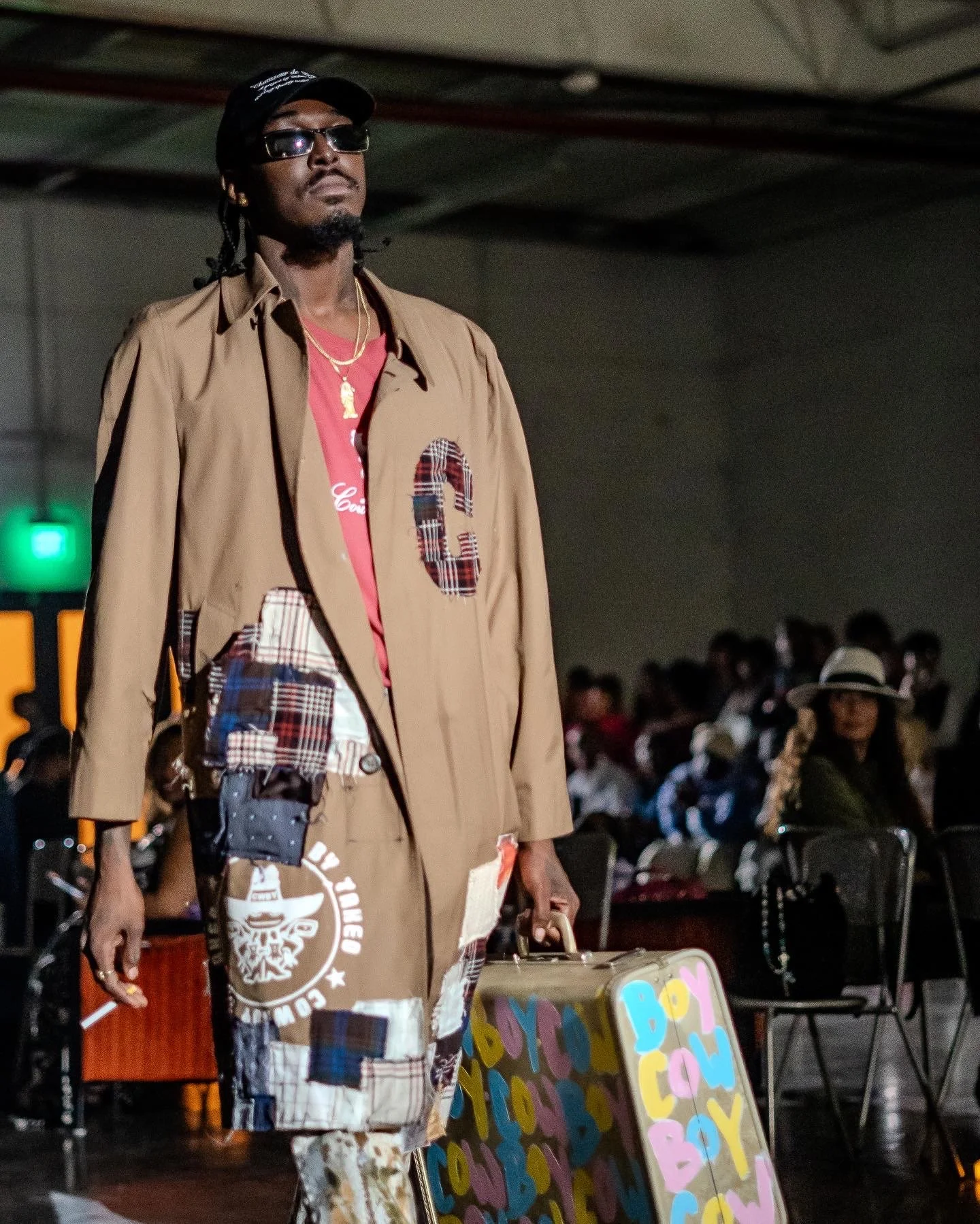 A man walking with a suitcase labeled 'BOY' in a crowded indoor space.