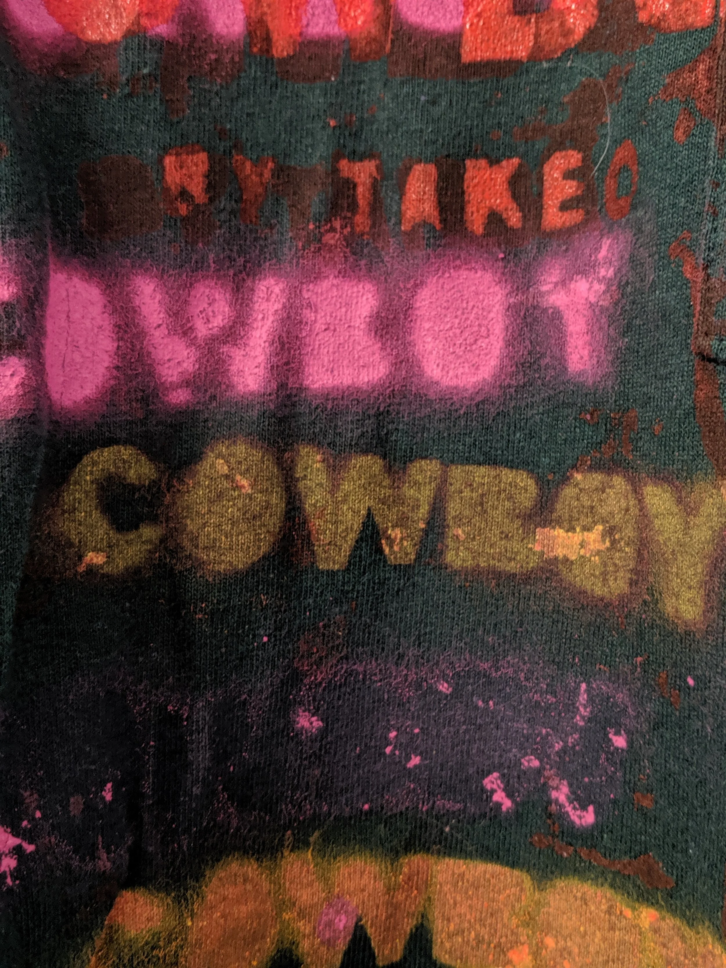 Close-up of a colorful, graffiti-style T-shirt with text in various colors saying 'ALL MY LOVE' and other partially visible words, with pink, green, red, and orange spray paint effects.