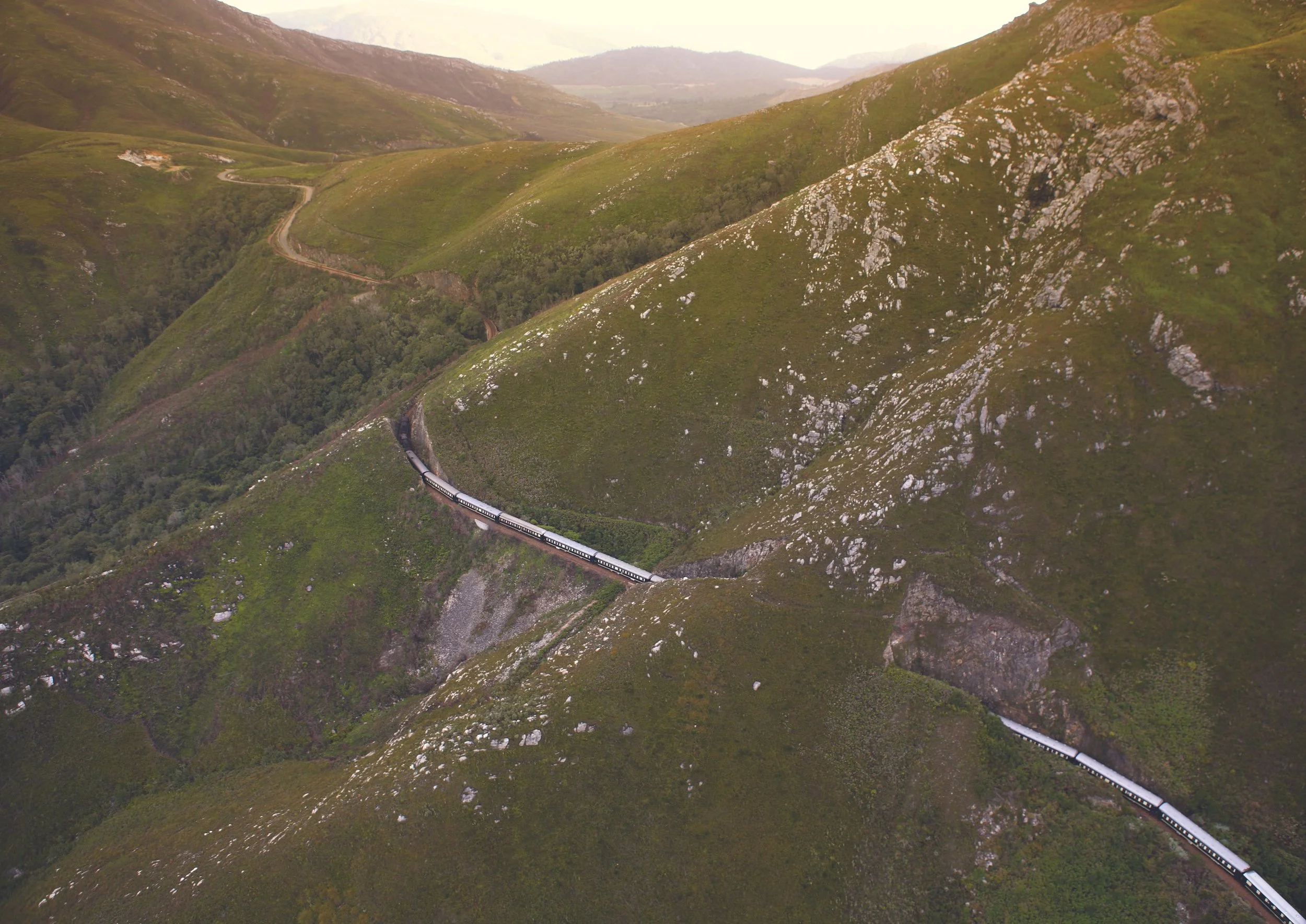 A train traveling through green, mountainous hills with a winding track.