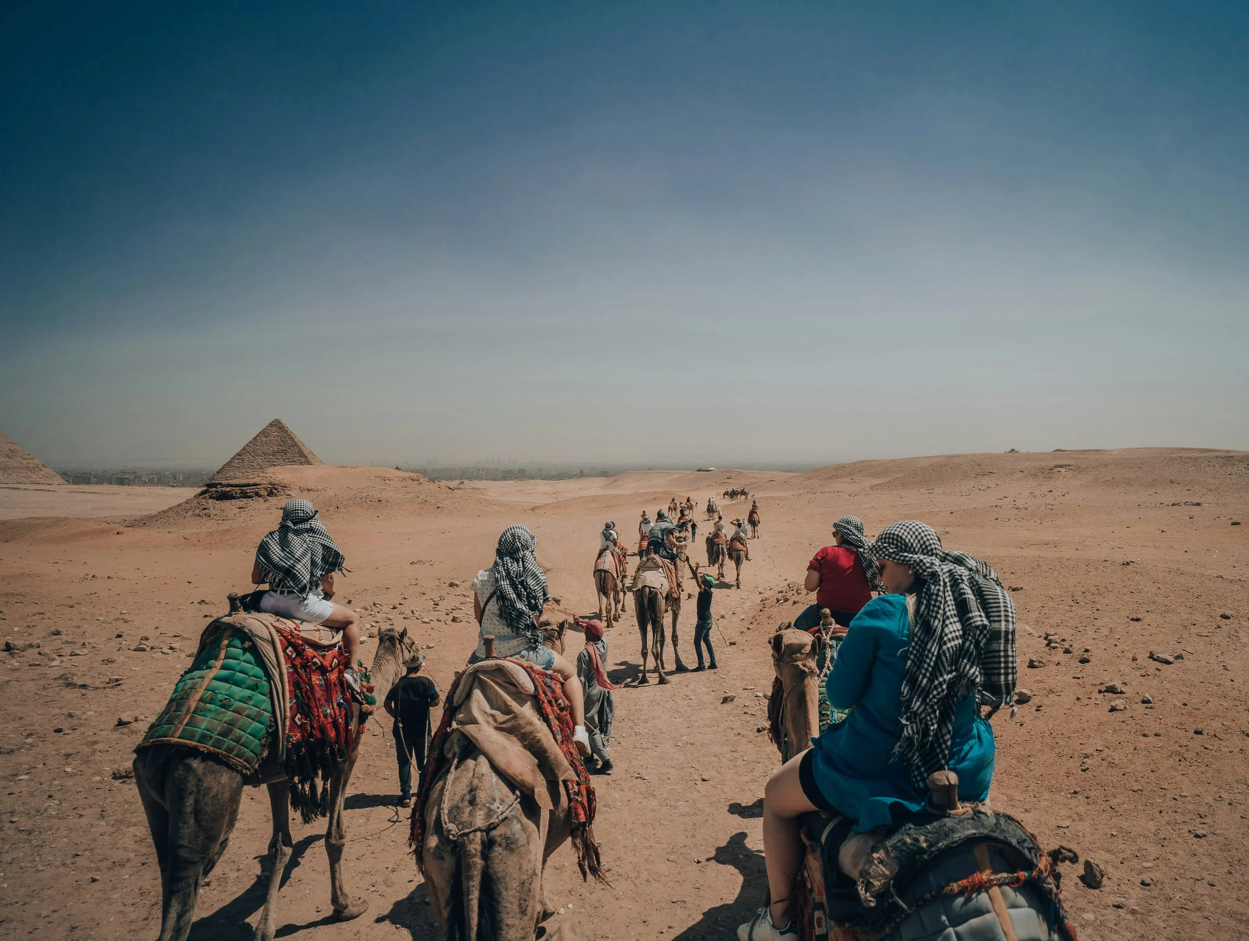 Tourists riding camels across a desert in Egypt with pyramids in the background.