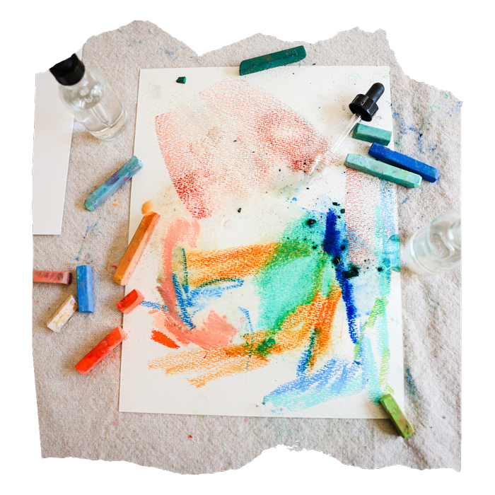 Colorful abstract chalk drawings on white paper with chalk pastel sticks, a dropper, and glass bottles on a fabric surface.