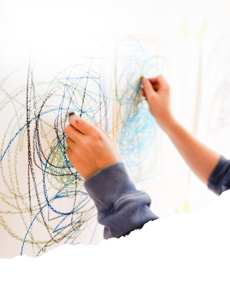 Child drawing with colored markers or crayons on a wall, creating abstract scribbles.