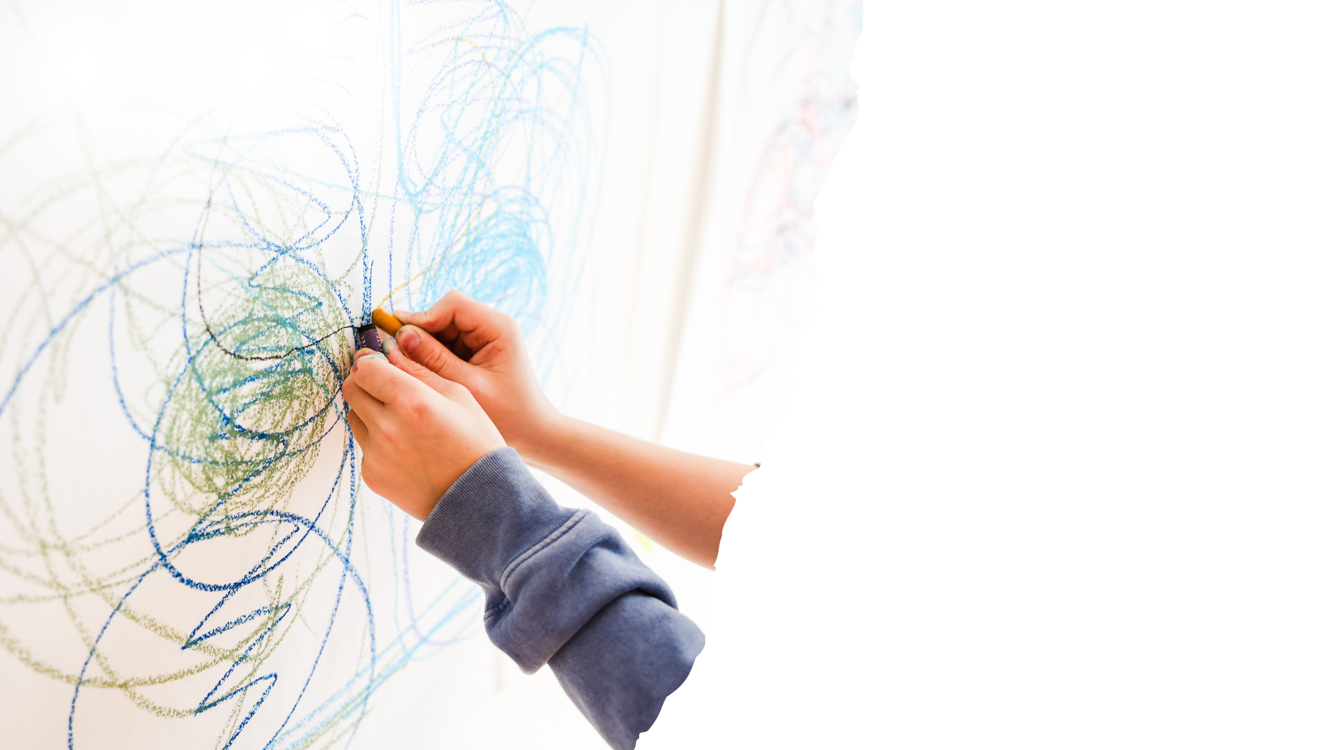 Child drawing on a whiteboard with colored chalk, creating messy, colorful scribbles.