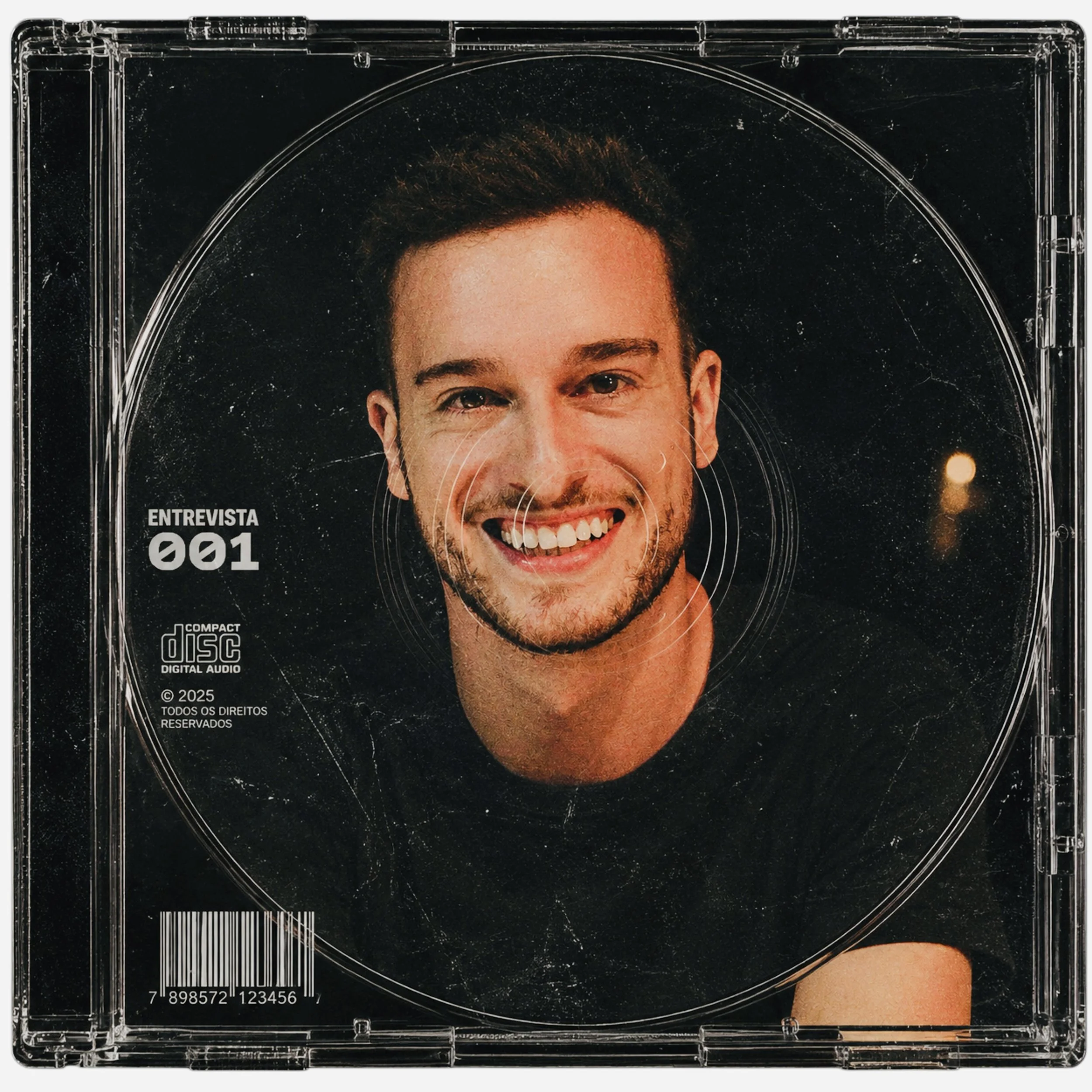Parte de uma capa de uma revista ou booklet com uma foto sorridente de um homem de cabelo curto e barba, com fundo preto e detalhes de círculos e linhas. Texto na capa inclui 'ENTREVISTA' e '001'.