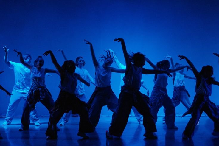 Grupo de dançarinos realizando uma coreografia no palco com iluminação azul.