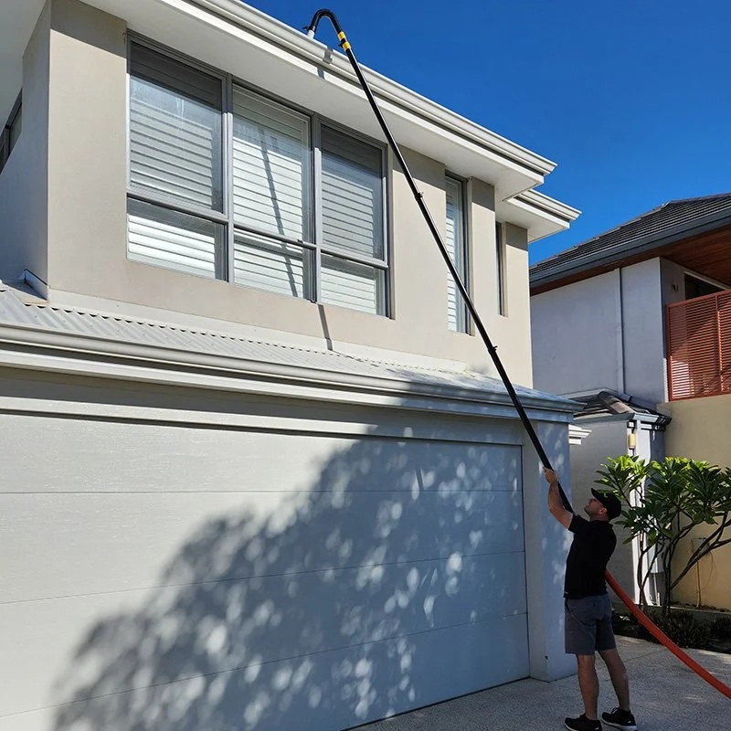 A man cleaning upper storey gutters with extended pole using a gutter vacuum system.