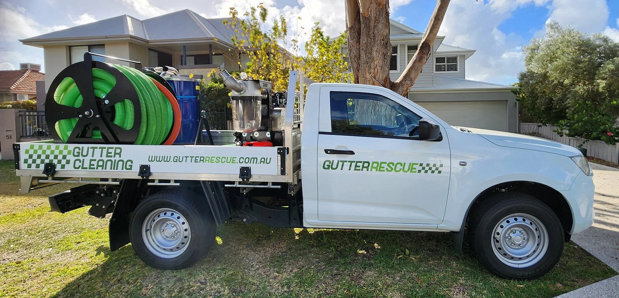 A white truck with Gutter Rescue branding on the side, parked in front of a house, equipped with gutter cleaning equipment including hoses, debris collection, and tools for cleaning gutters.