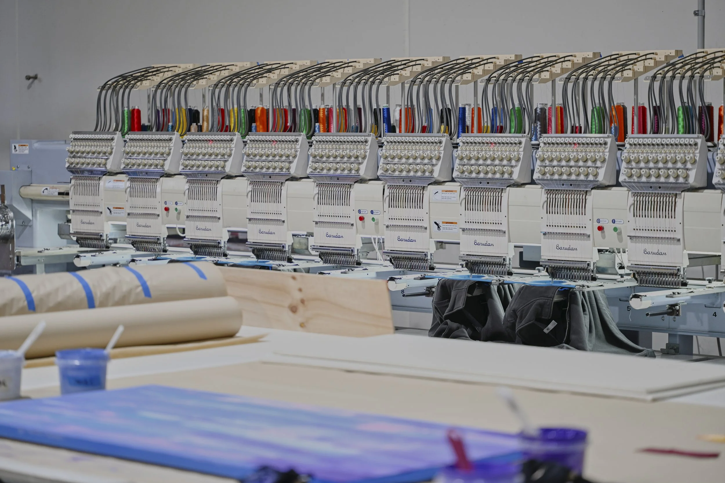 Industrial embroidery machines with colorful threads in a factory setting.