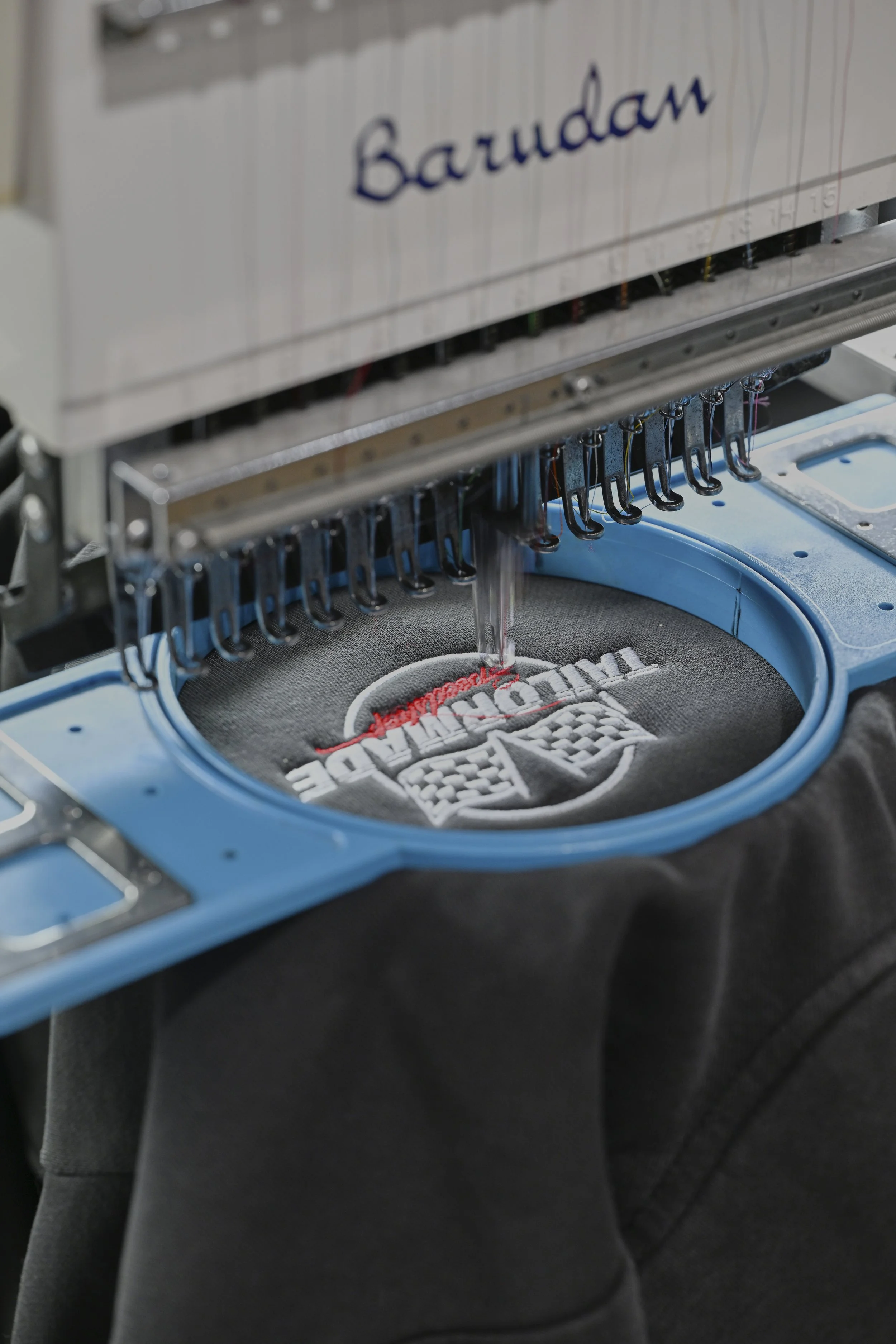 Close-up of embroidery machine stitching a logo onto black fabric.