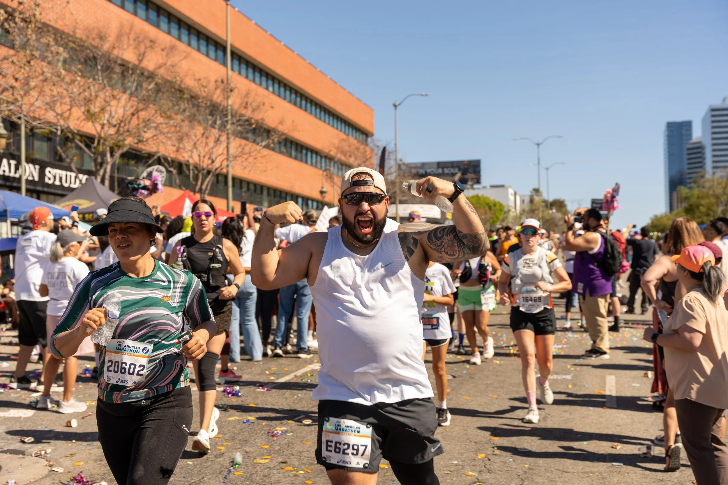People participating in a marathon race outdoors on a sunny day, with some smiling and celebrating.