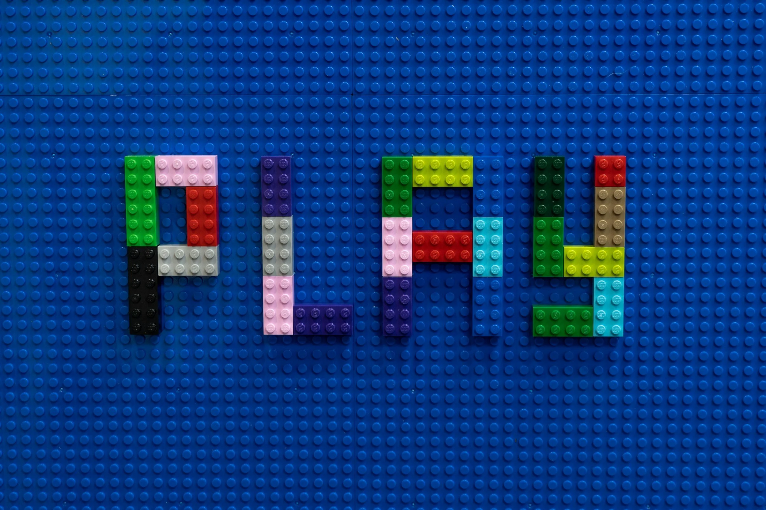 Colorful LEGO bricks spelling out the word 'PLAY' on a blue background.