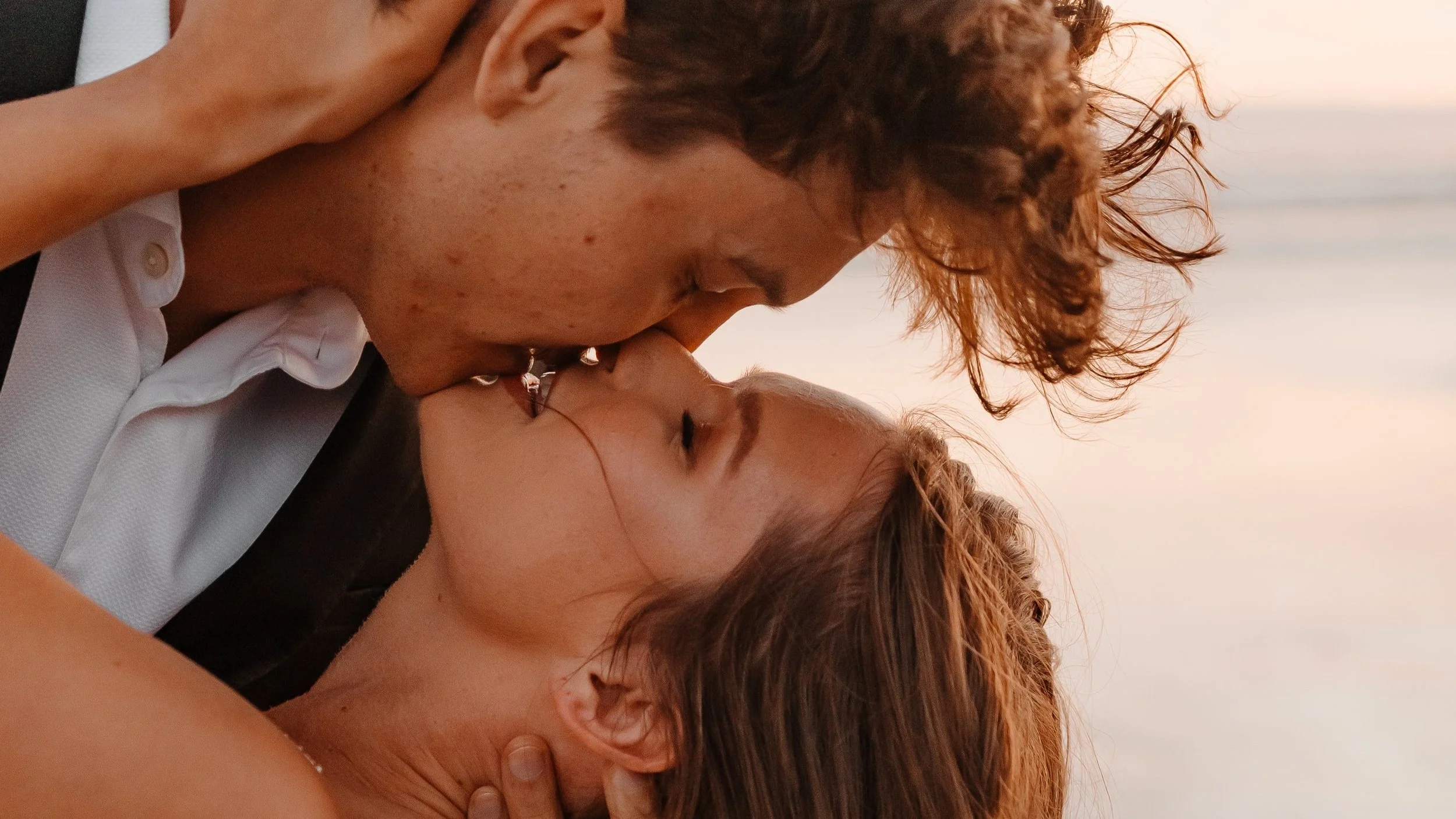 Close-up of a couple kissing passionately at sunset on the beach.