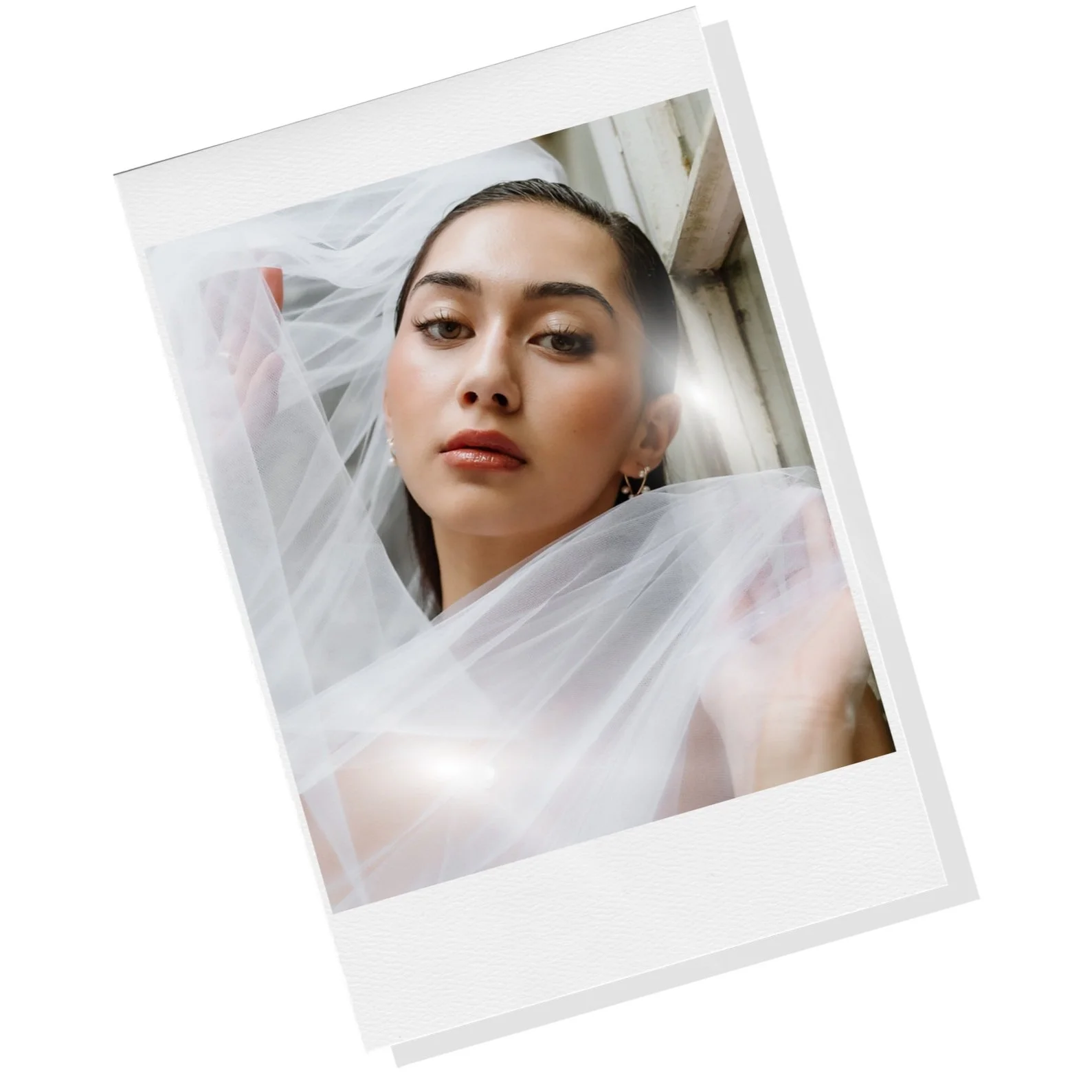A close-up portrait of a woman with dark hair, wearing a white sheer fabric or veil, leaning near a window with visible wooden window frame and natural light shining on her face.