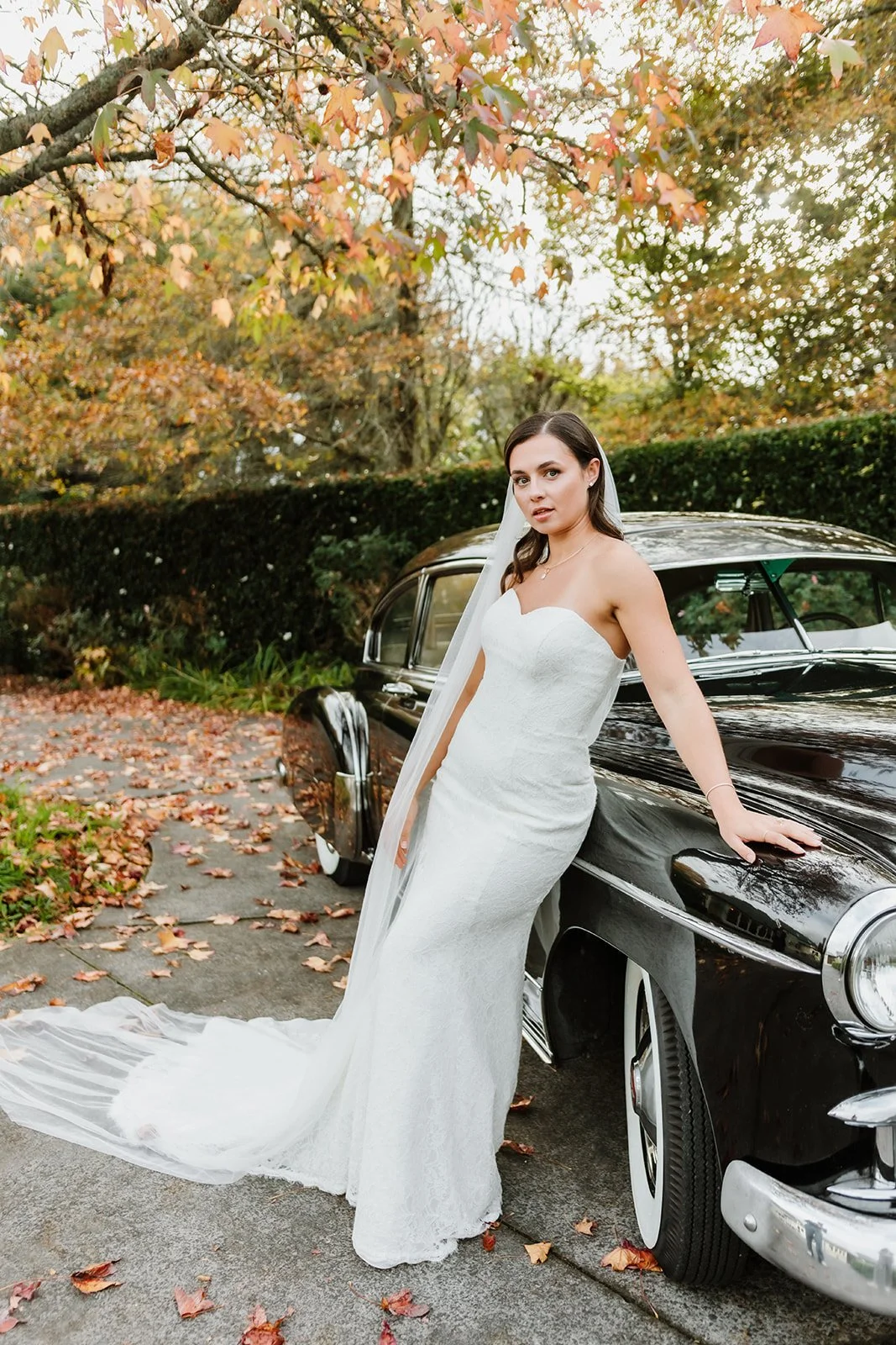 Bride with soft glam makeup standing next to vintage car in wedding dress with long veil, Wavey hair, Hollywood waves. Glam makeup. pretty girl.