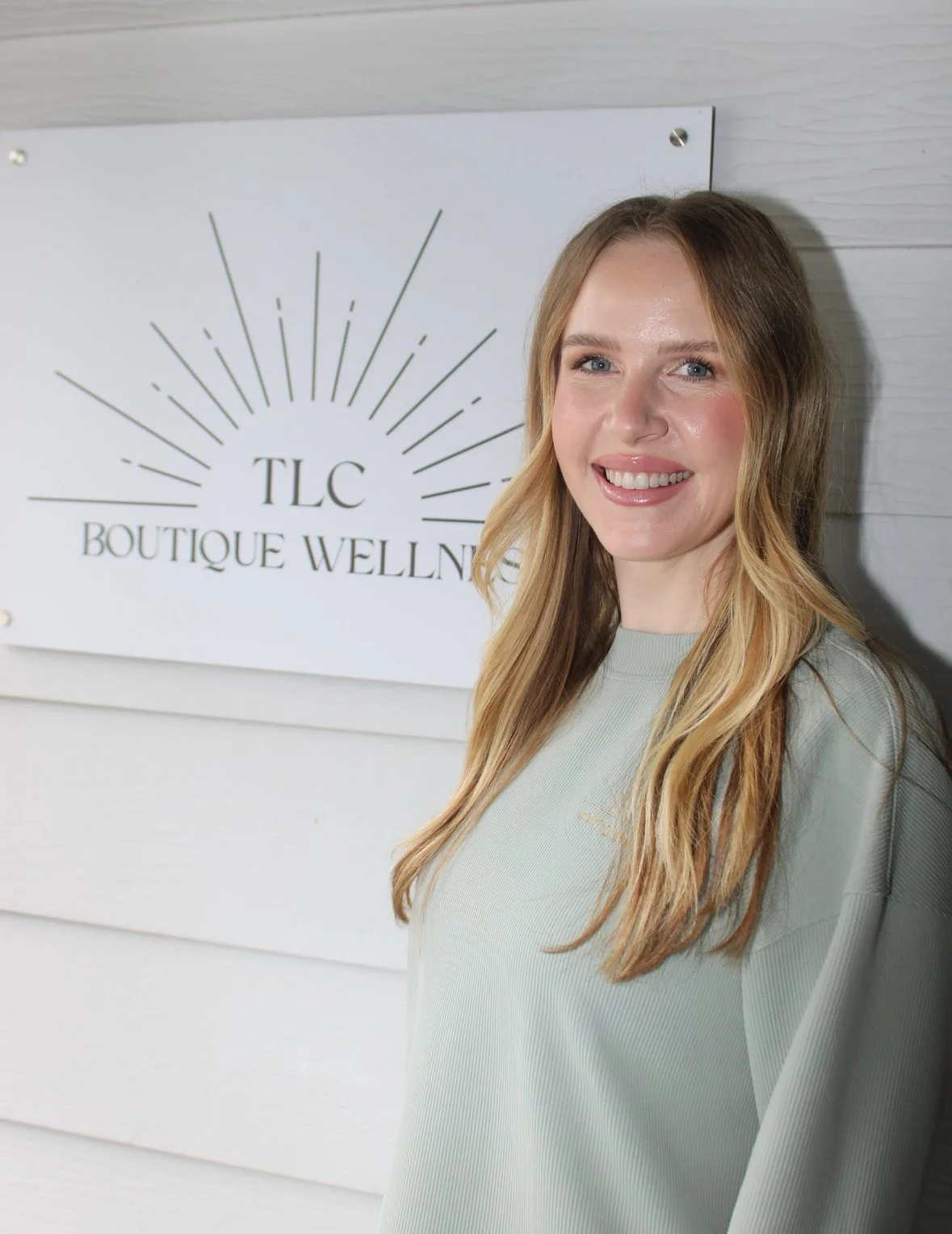 A woman with long dark hair wearing a navy sleeveless dress and a brown belt, standing against a plain white background.
